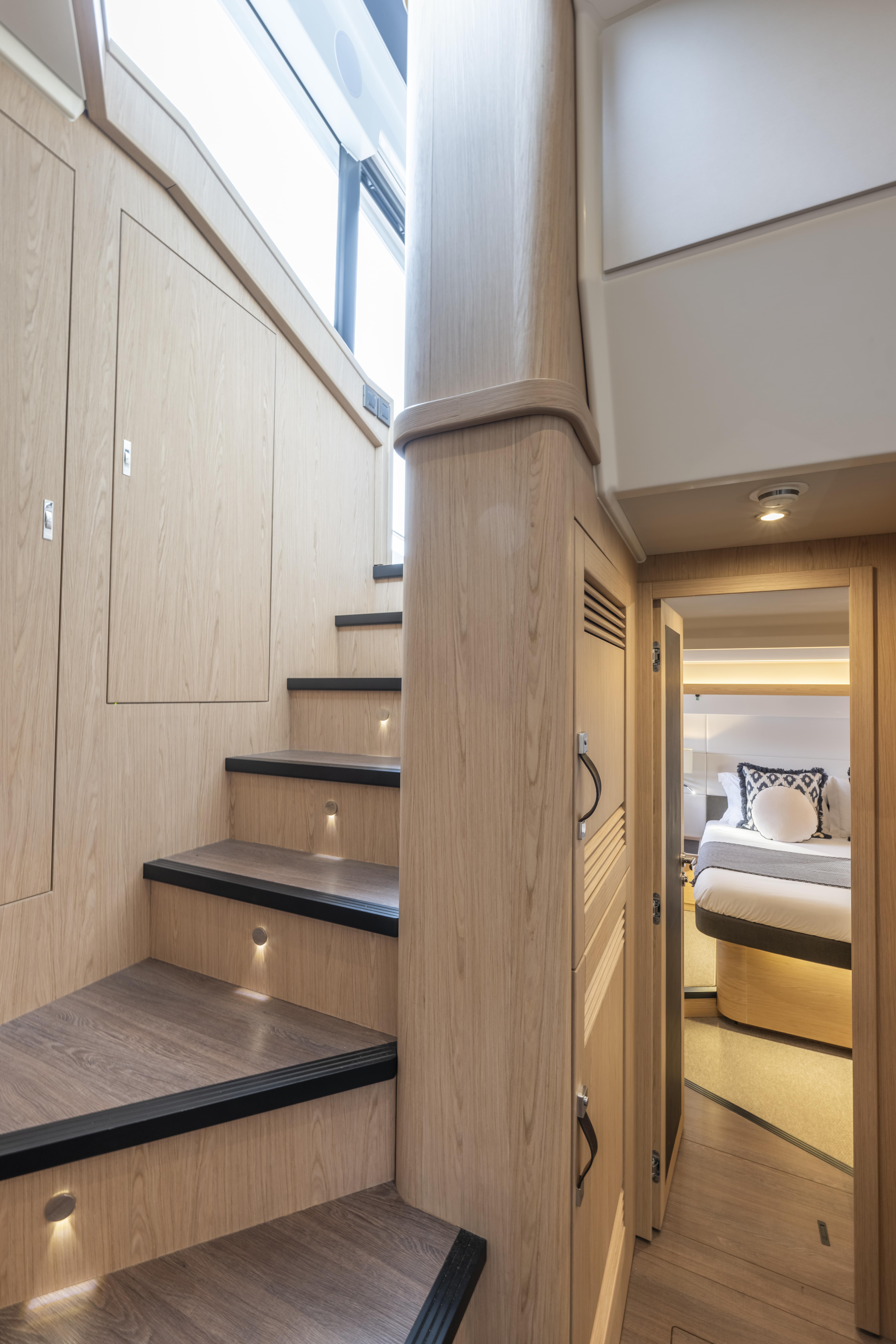 Interior of 2026 Beneteau Swift Trawler 54, featuring wooden stairs and a cozy bedroom.