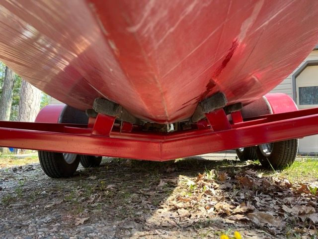Underside of a red boat on a trailer, surrounded by leaves and trees.