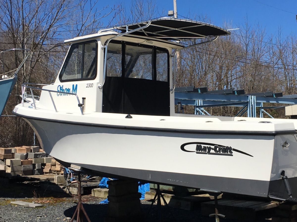 A 2015 May-Craft 2300 Pilot boat is on a stand. It features a covered pilothouse.
