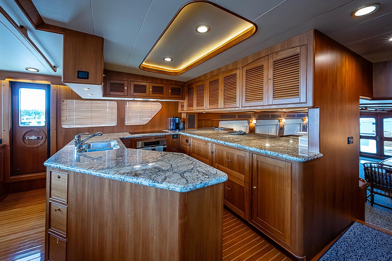 Luxurious kitchen interior of 2014 Marlow 80 Explorer yacht with wooden cabinetry and granite countertops.