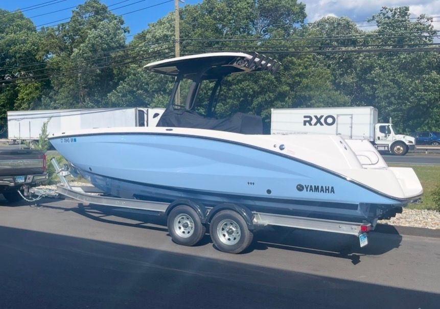 A 2024 Yamaha 255 FSH Sport H on a trailer, featuring a blue hull and black T-top.