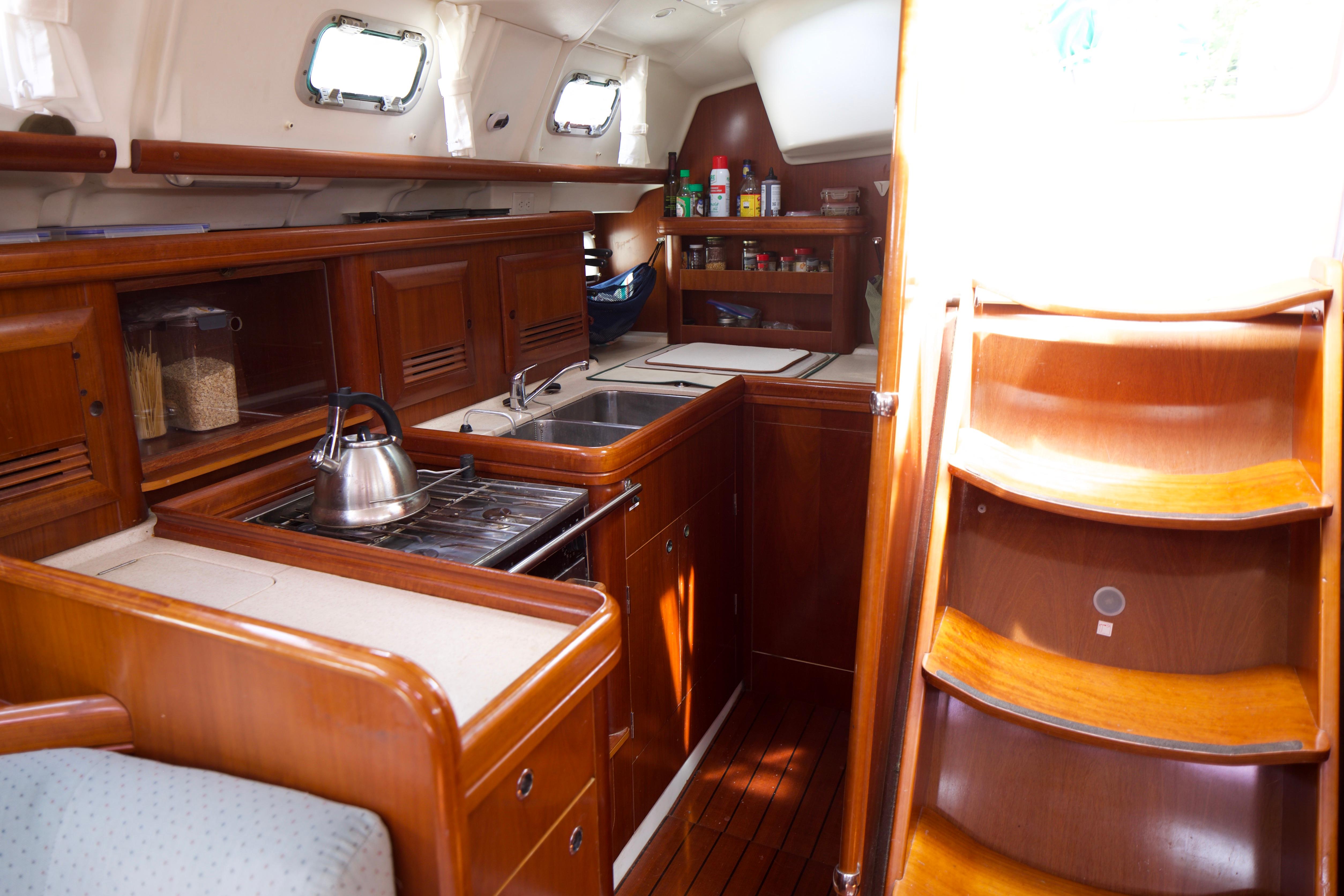 Interior of 2005 Beneteau 423 yacht kitchen with wooden cabinetry and stairs.