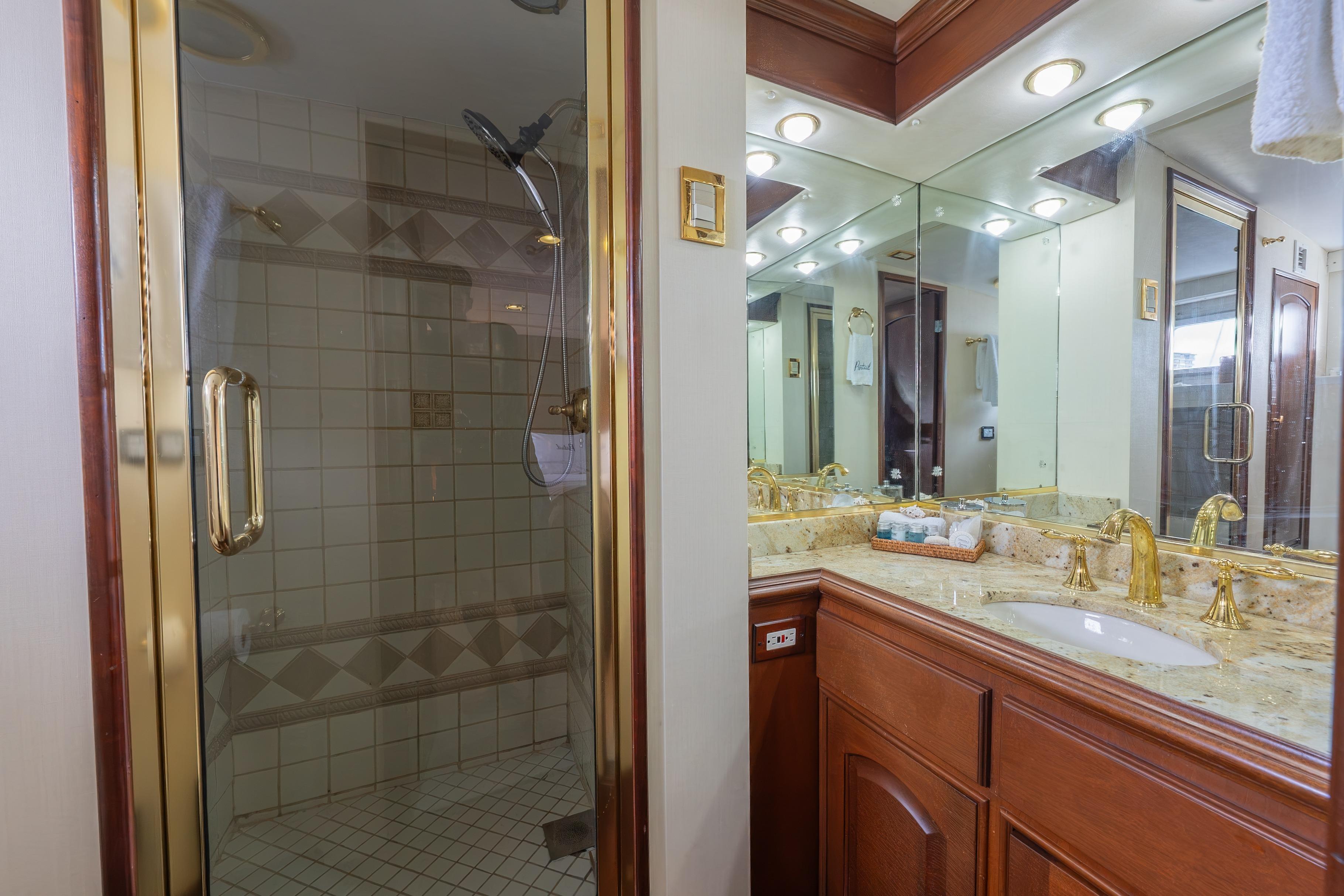 Luxurious bathroom with gold fixtures, large shower, and mirrors on a 1963 Trumpy Classic yacht.