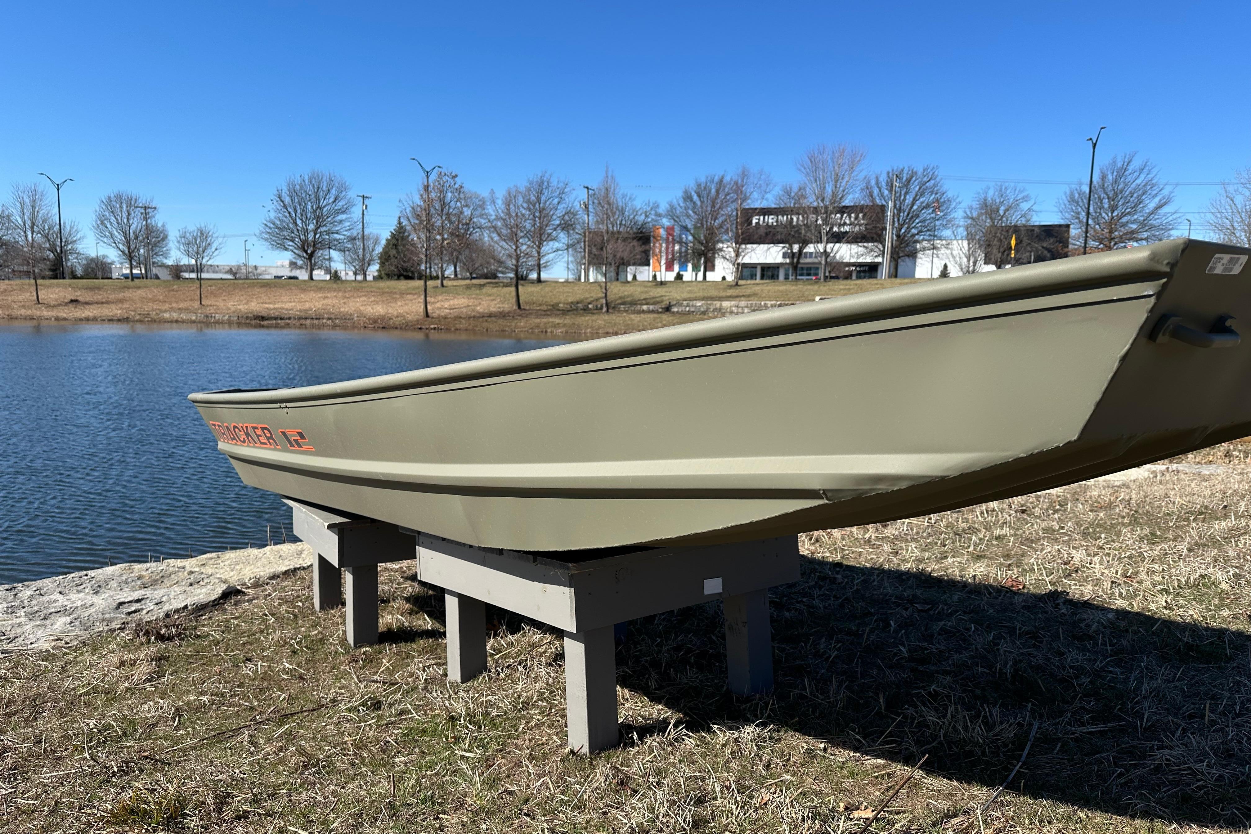 2026 Tracker Grizzly 12 Jon boat displayed near a serene lake under a clear blue sky.