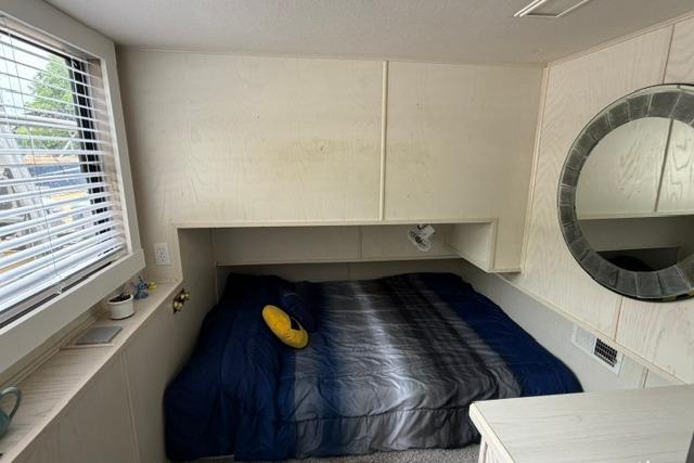 Cozy bedroom in 1997 Stardust Houseboat, featuring a bed, window, and round mirror.