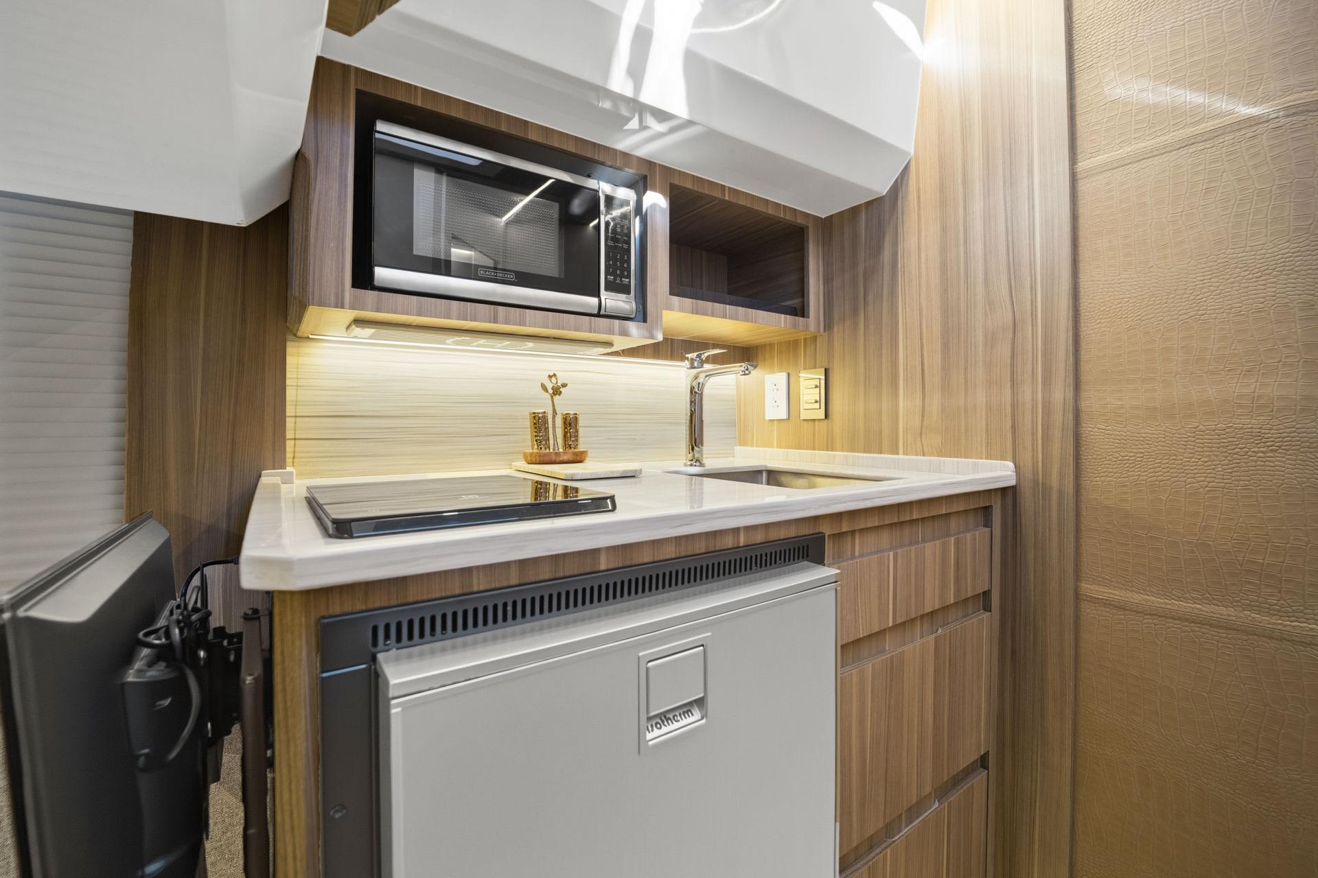 Compact kitchen in 2026 Hanover 447 RV with microwave, sink, and fridge.