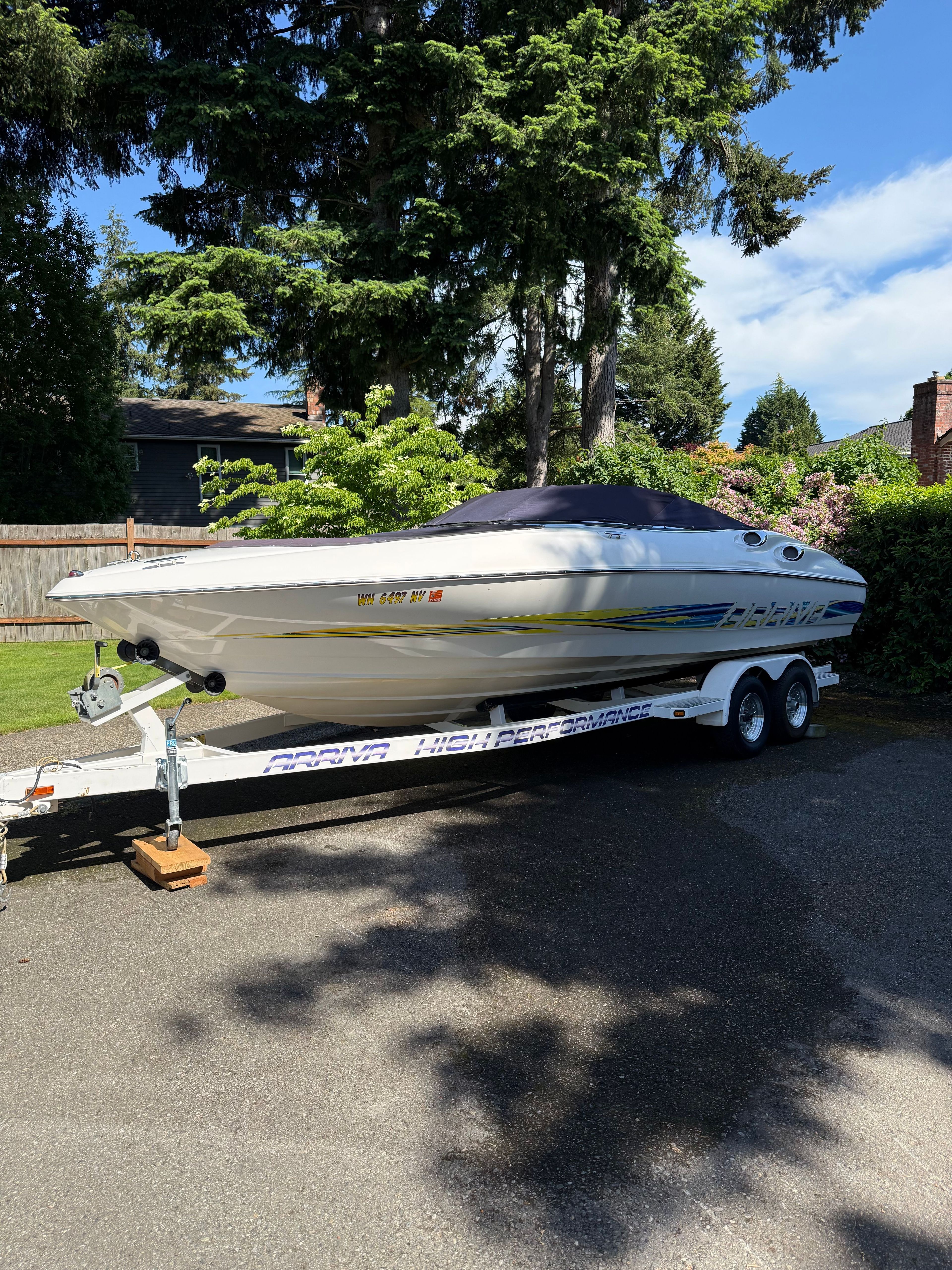A white 1997 Arriva 2550 motorboat on a trailer in a garden setting.