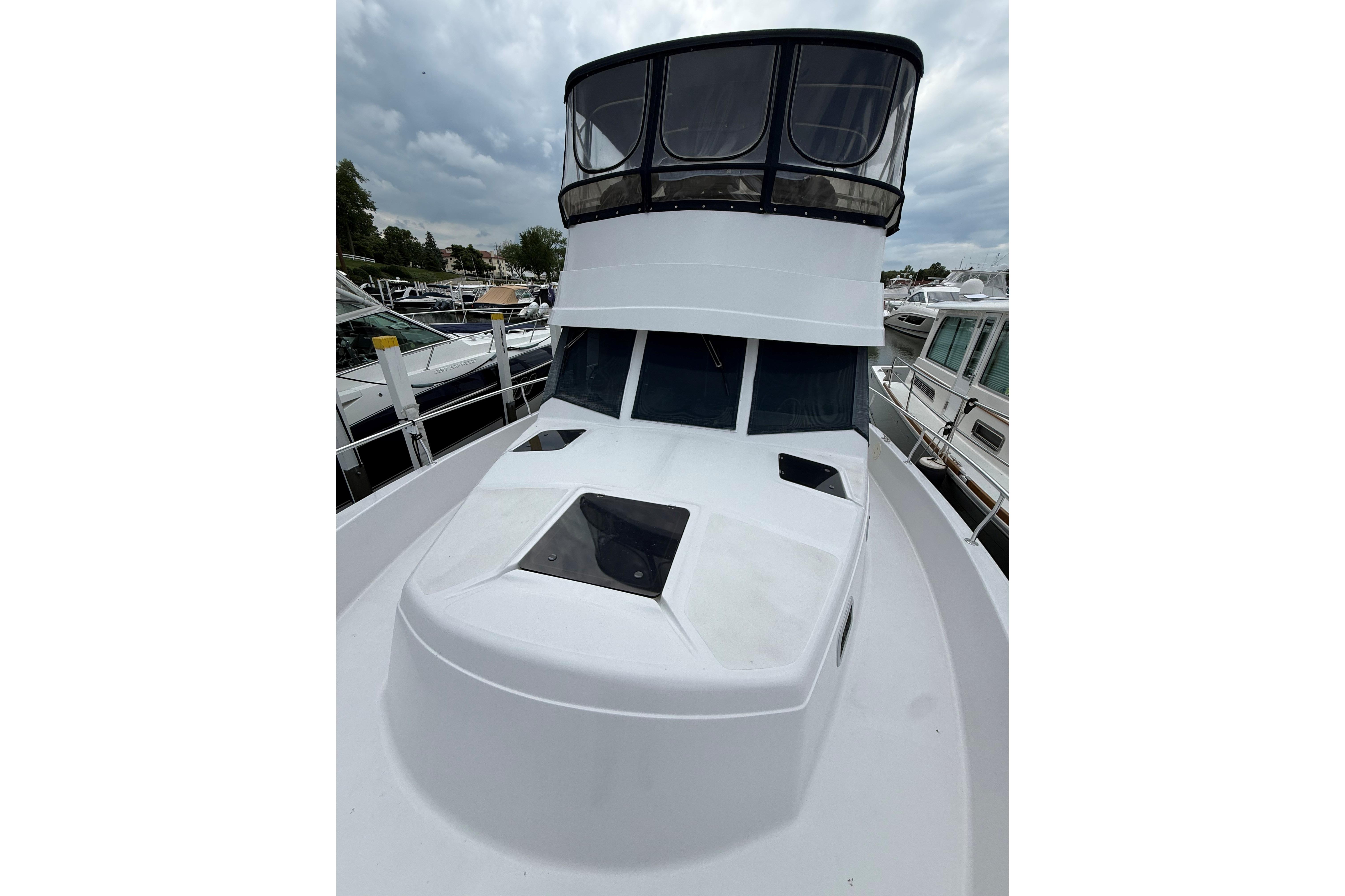 1999 Mainship 350 Trawler with enclosed flybridge, docked at marina under cloudy skies.