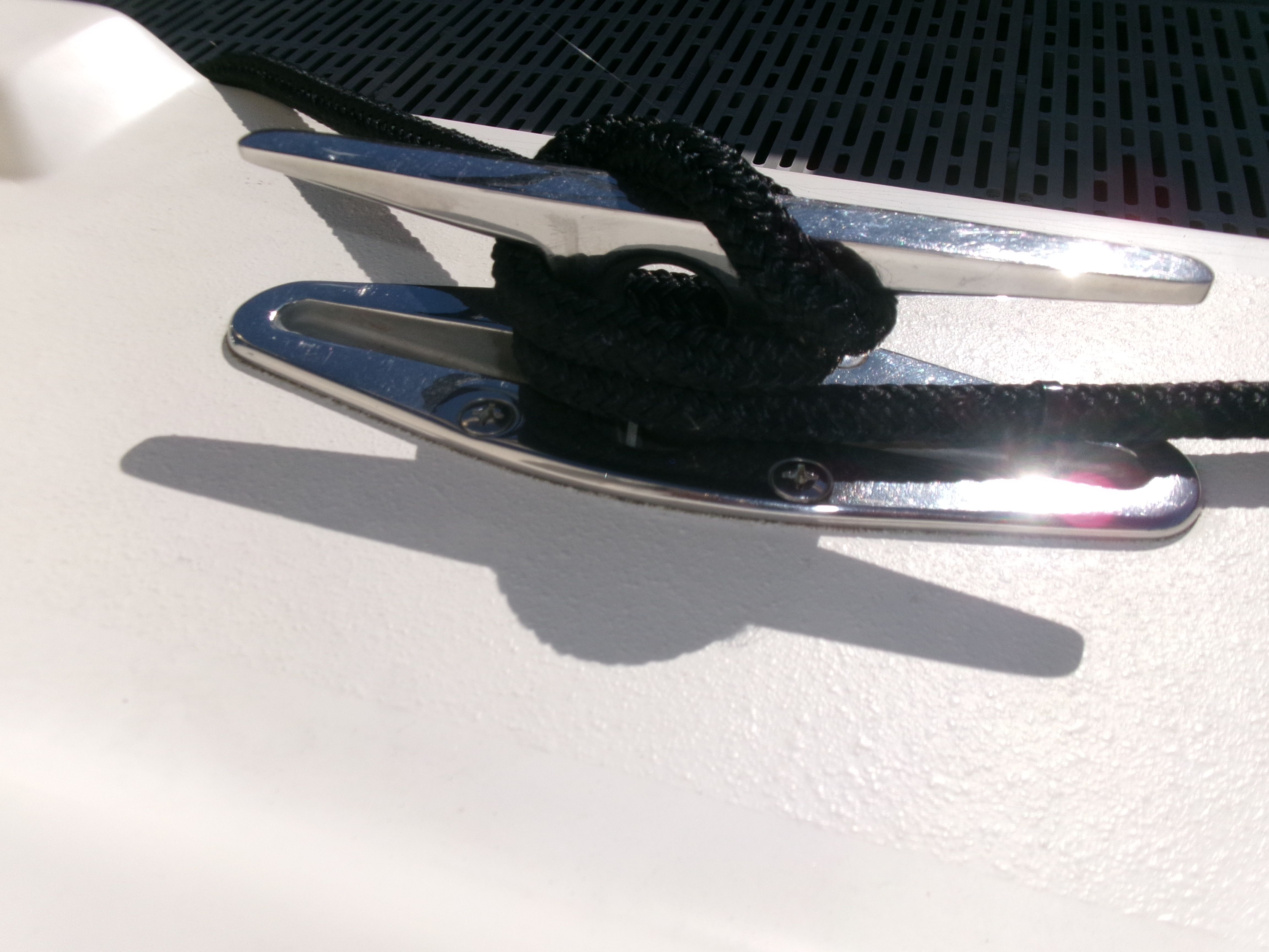 A silver boat cleat with a black rope on a white deck.