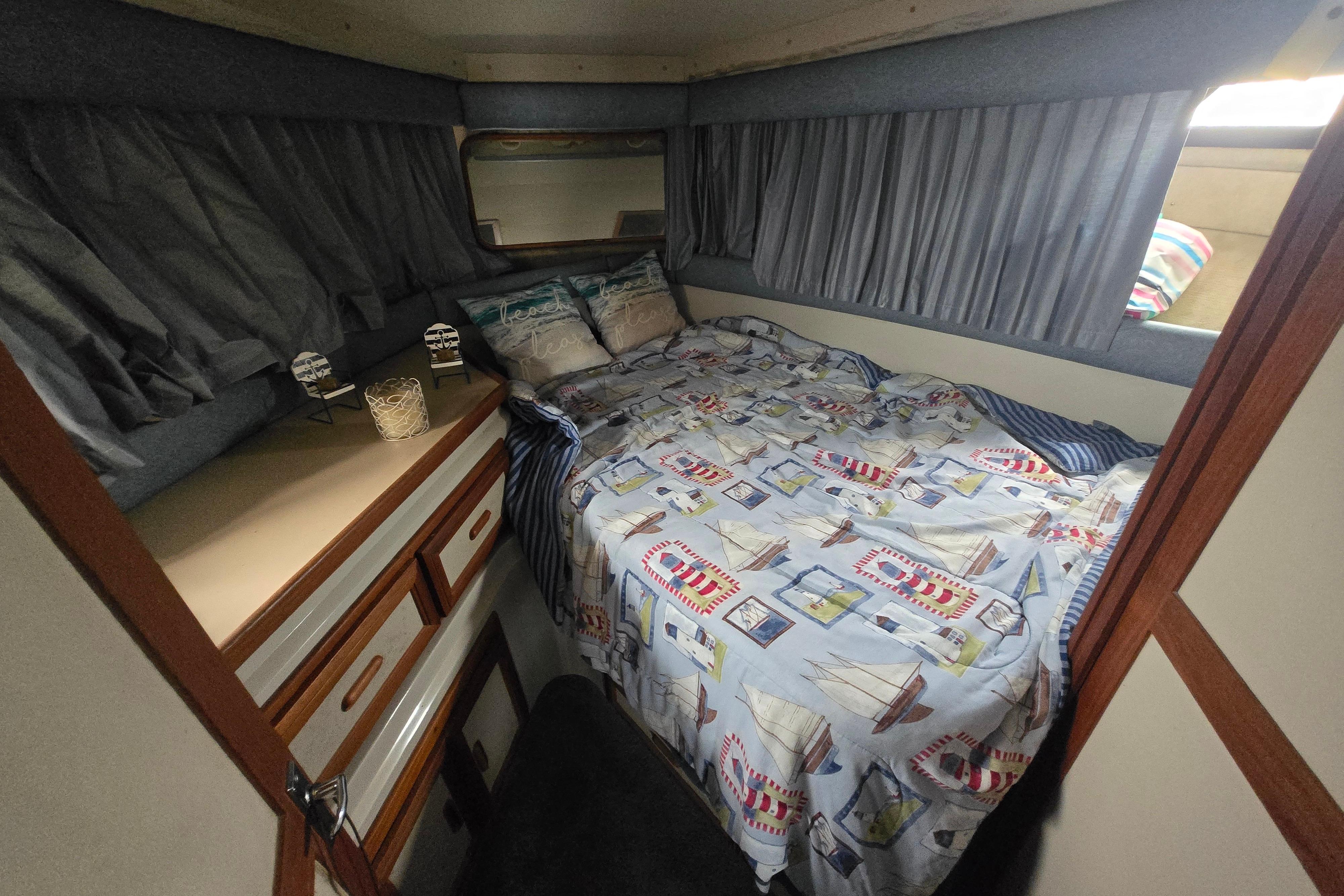 Cozy cabin interior of 1987 Carver 32 Mariner with nautical-themed bedding and storage.
