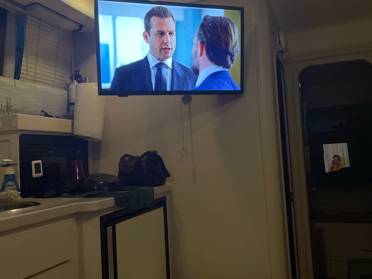 Interior of a yacht with a TV showing a scene. Kitchen area with microwave and sink.