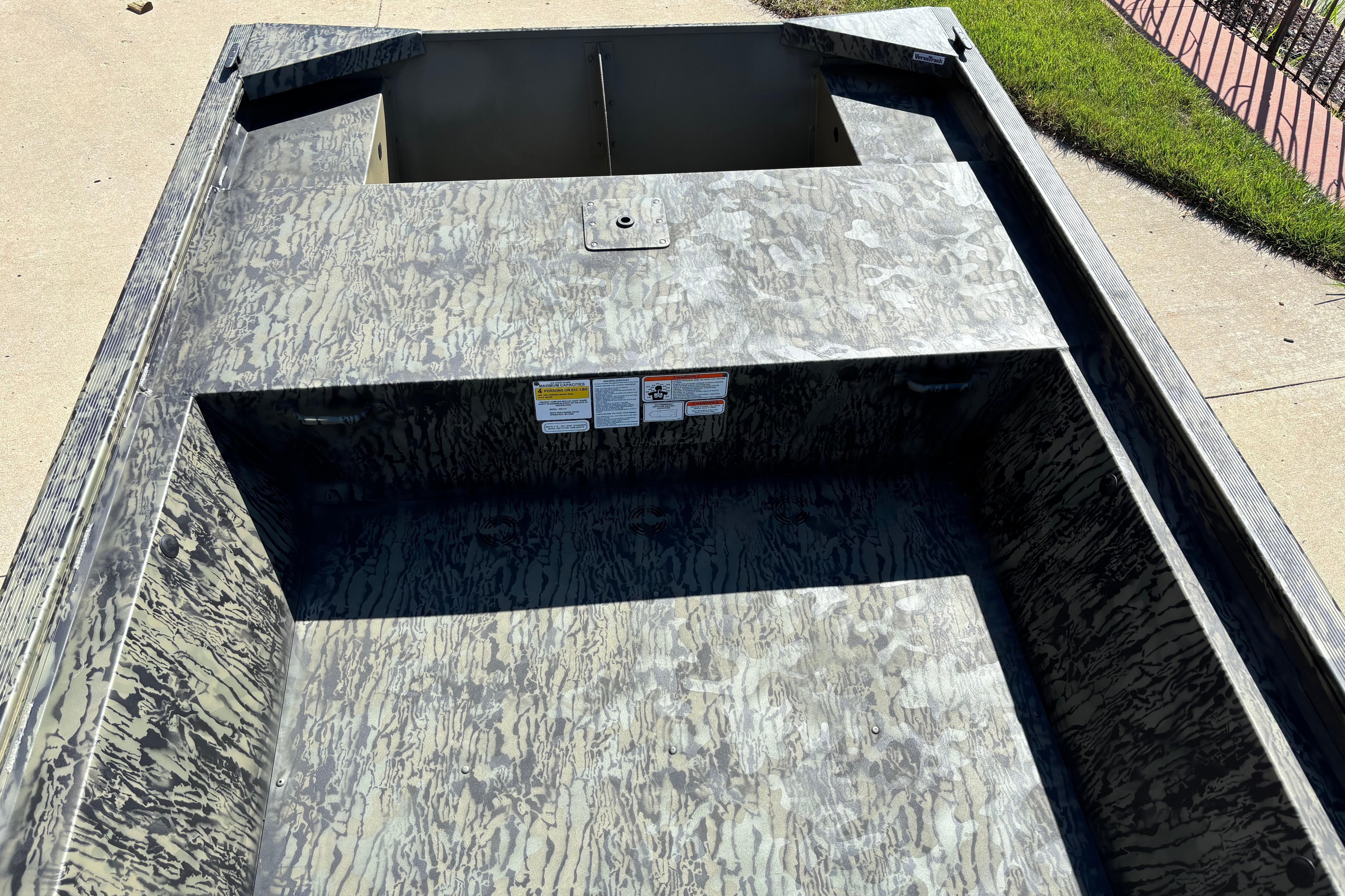 2026 Tracker Grizzly 1648 Utility boat interior with camouflage pattern, parked on concrete.