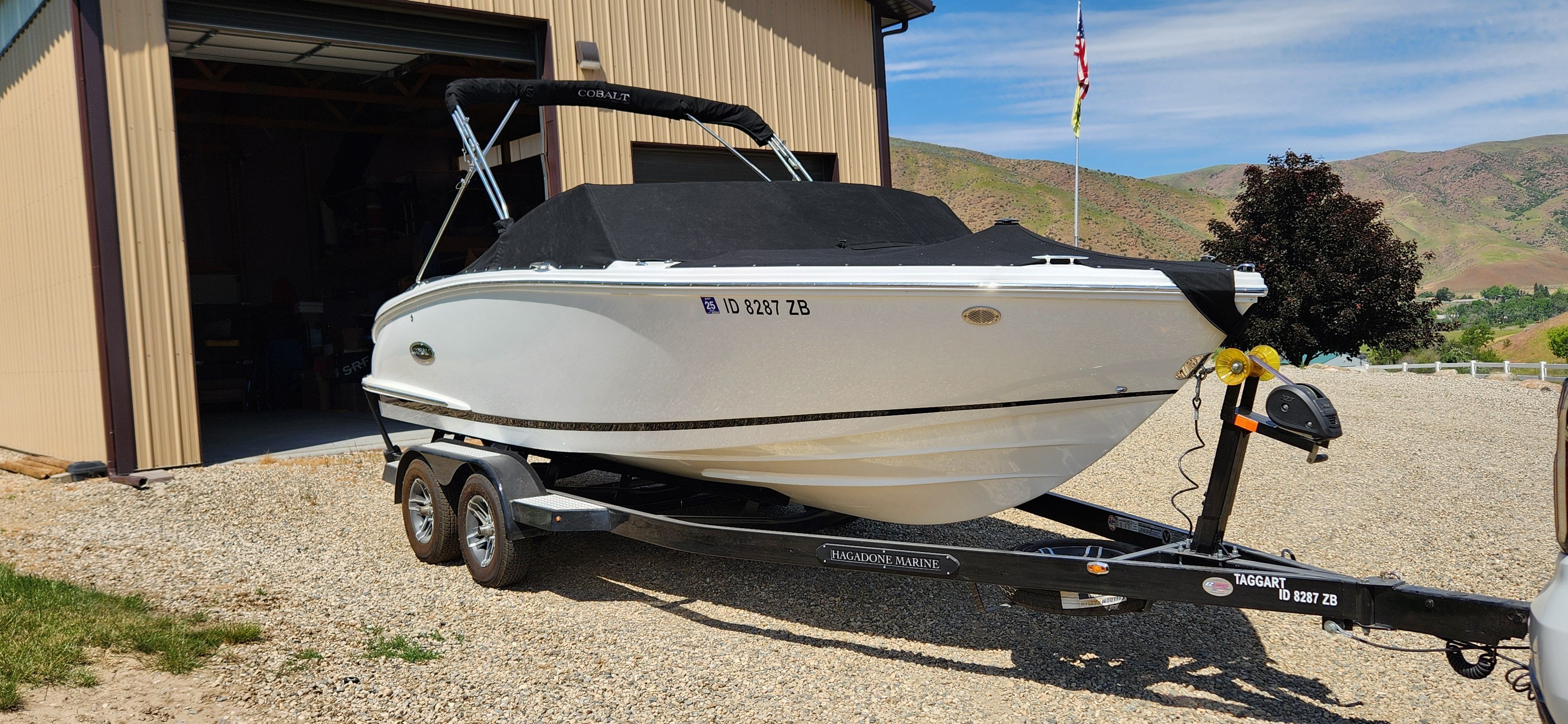 A white Cobalt CS22 boat on a trailer next to a garage.