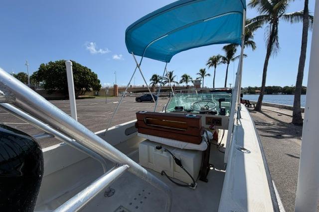 1990 Boston Whaler 17 Newport boat with blue canopy, parked near palm trees by the water.