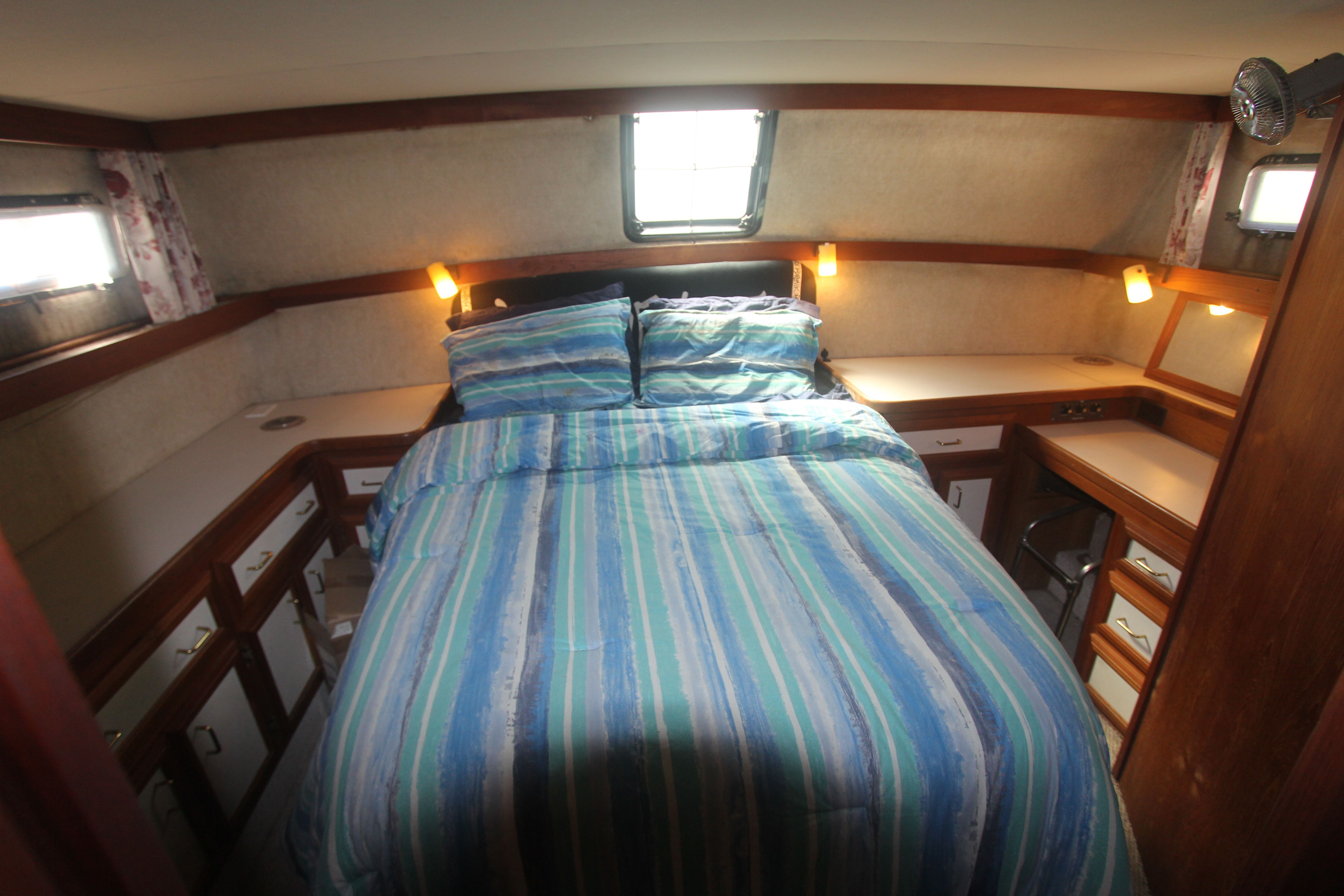 The image shows a cozy cabin with a double bed, surrounded by wooden cabinets and windows.