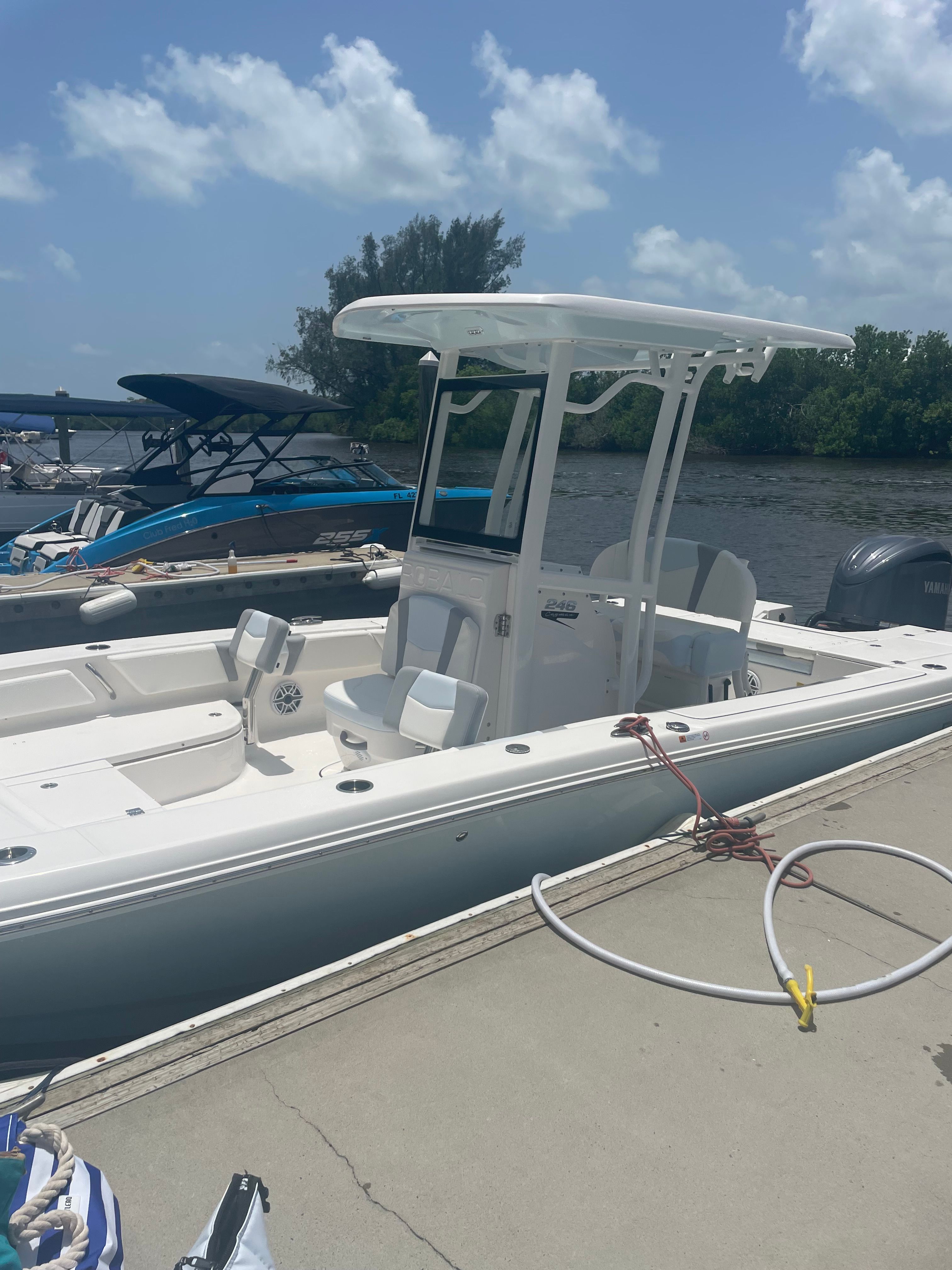 A white boat docked, featuring a T-top and seating, under a clear blue sky.