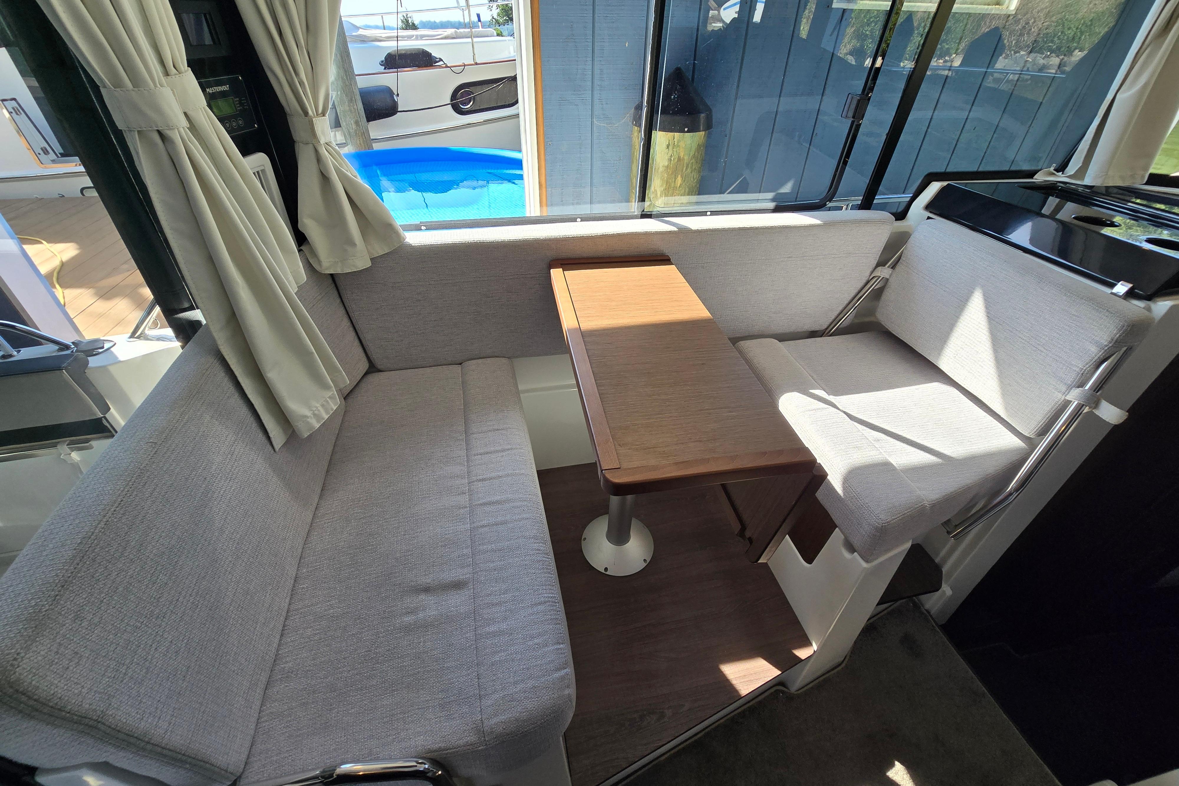 Interior of Jeanneau NC Sport 895 with gray upholstery and wooden table.
