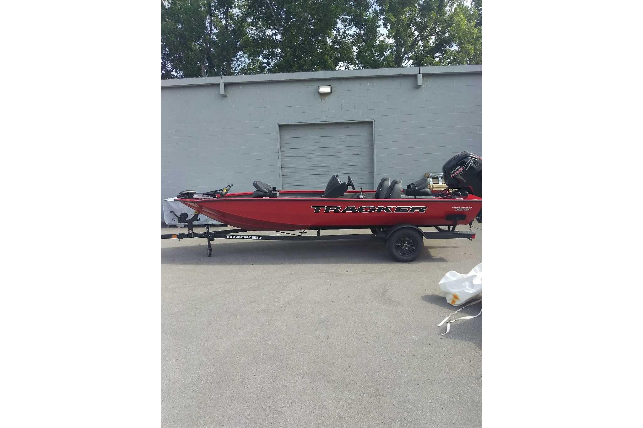 2026 Tracker Pro Team 190 boat, red, parked outdoors near a gray building.
