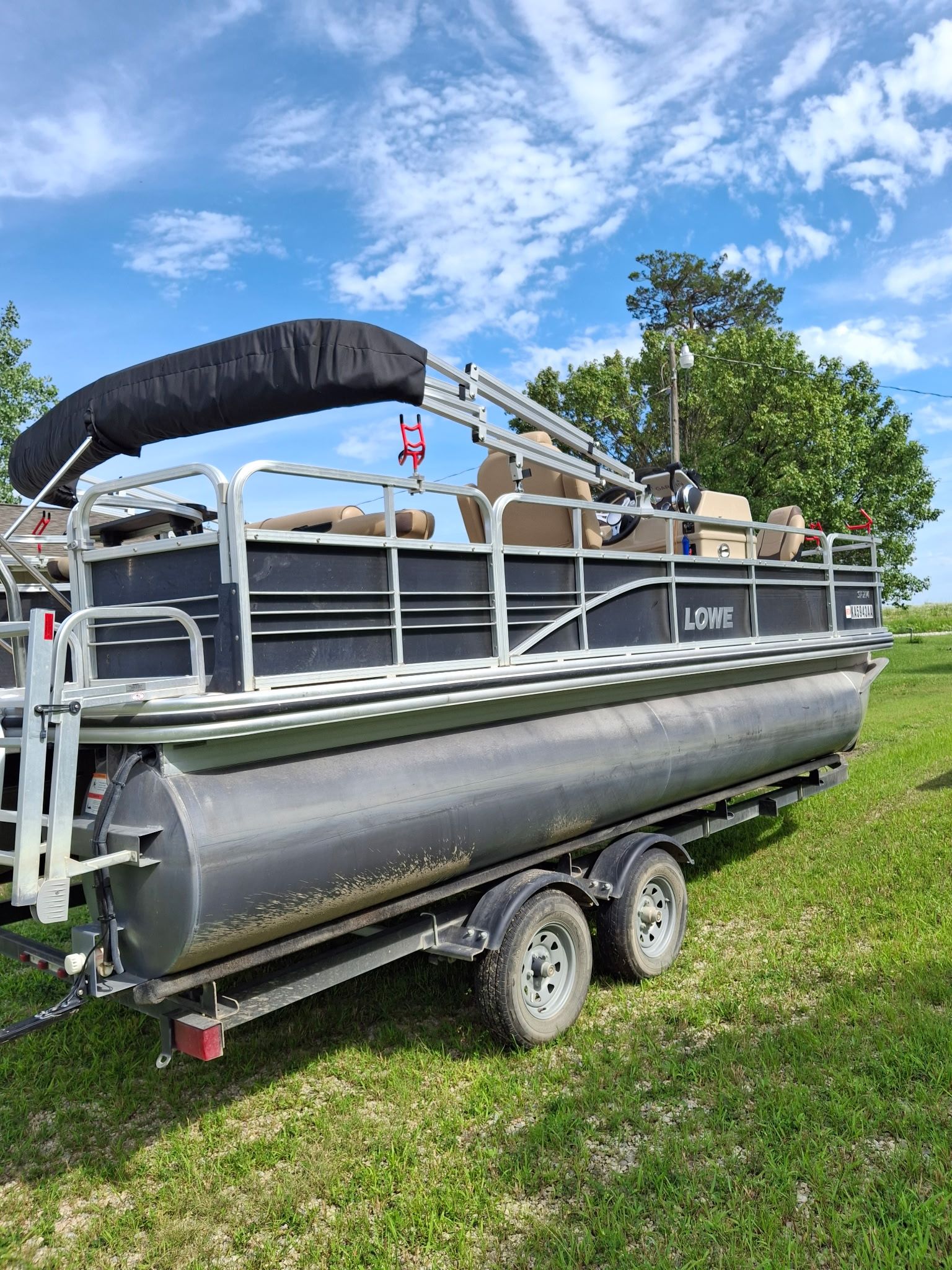 A Lowe SF 214 Sport Fish pontoon boat on a trailer in a grassy area.