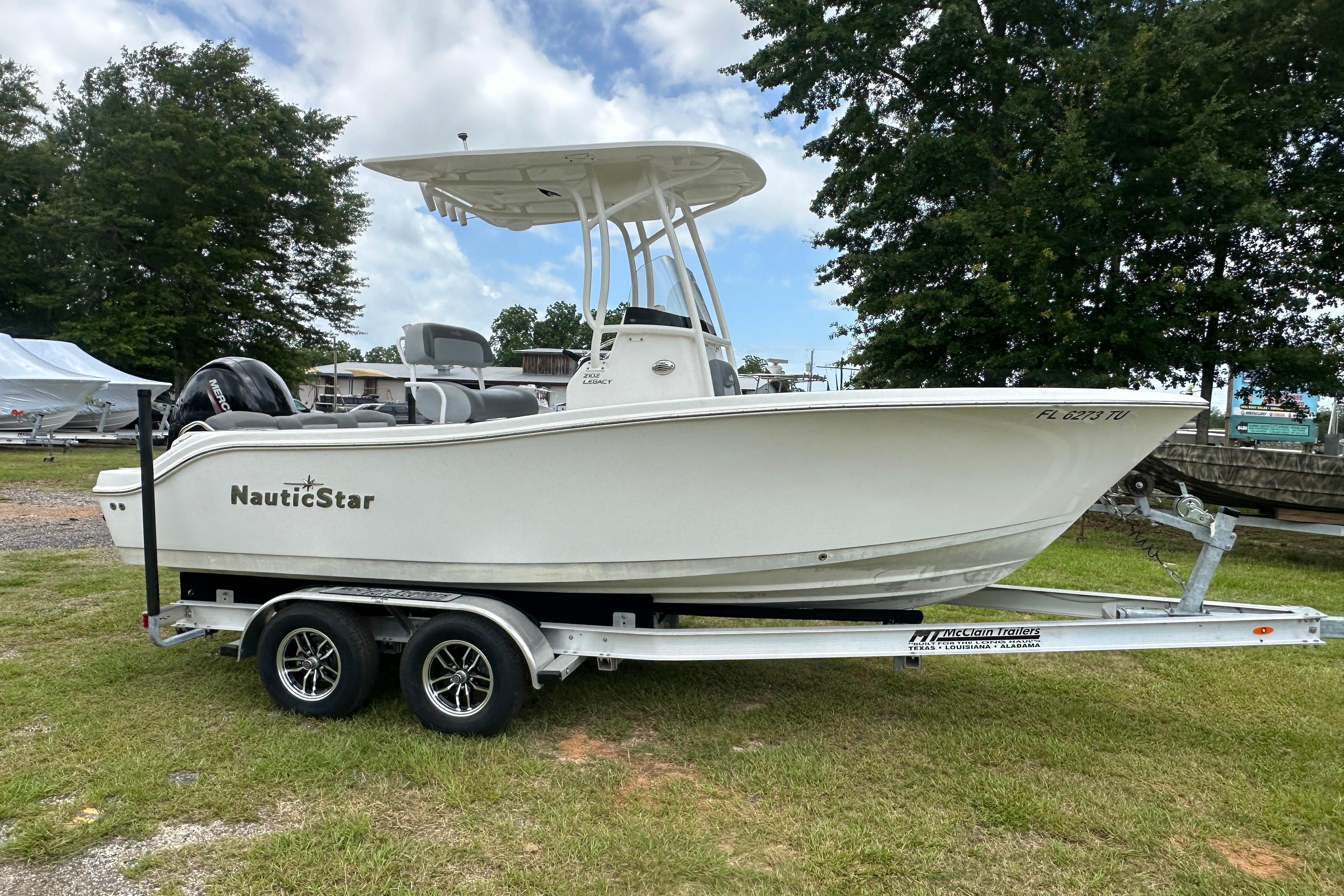 2023 NauticStar 2102 Legacy boat on trailer, parked on grass with trees in background.