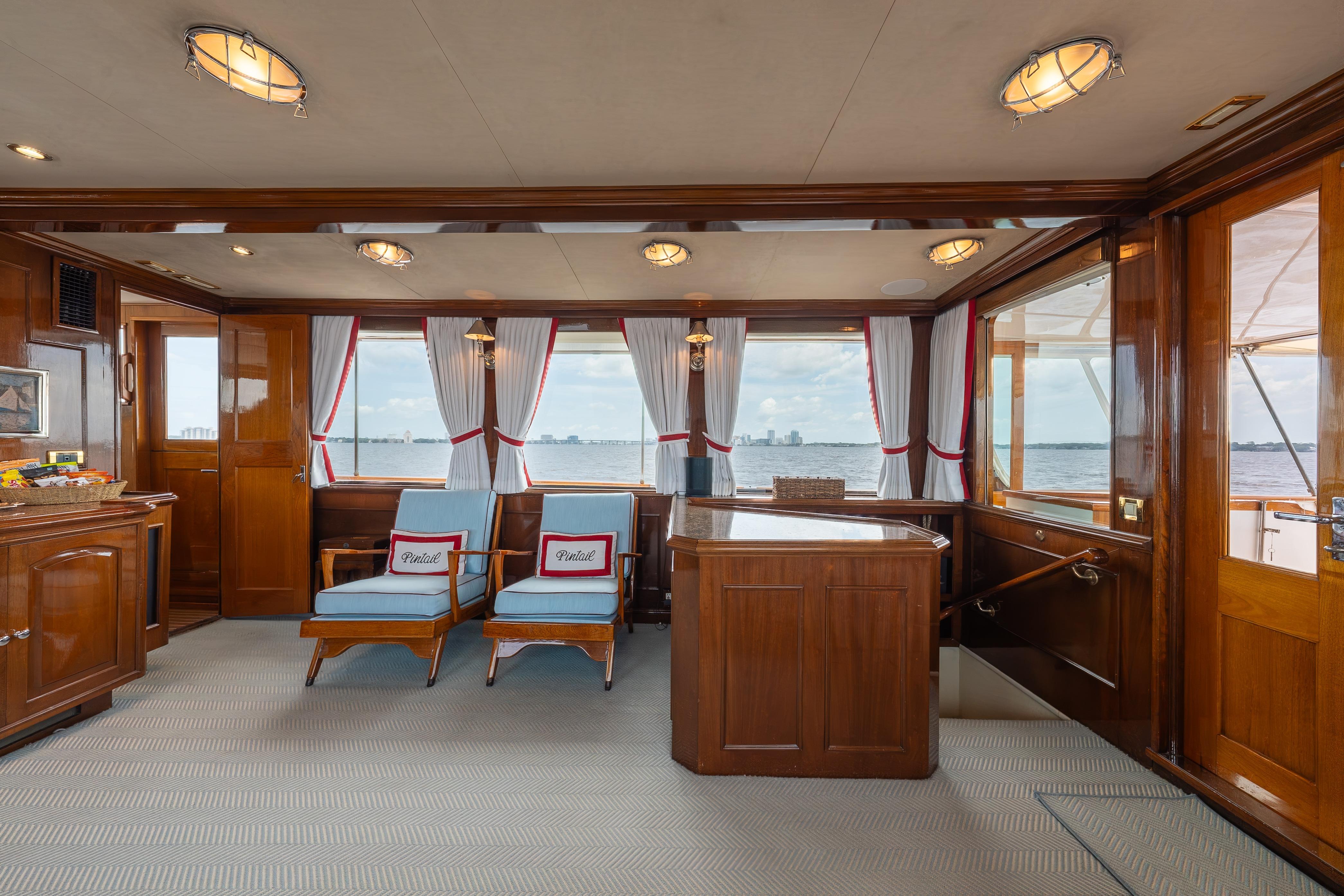 Interior of a 1963 Trumpy Classic yacht with wooden furnishings and large windows.