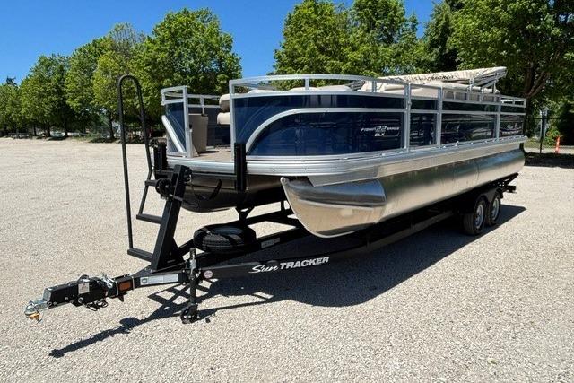2025 Sun Tracker Fishin' Barge 22 DLX pontoon boat on trailer, parked outdoors.