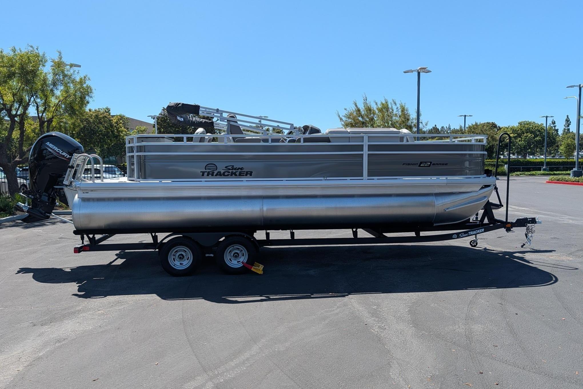 2026 Sun Tracker Fishin' Barge 22 DLX pontoon boat on trailer in parking lot.