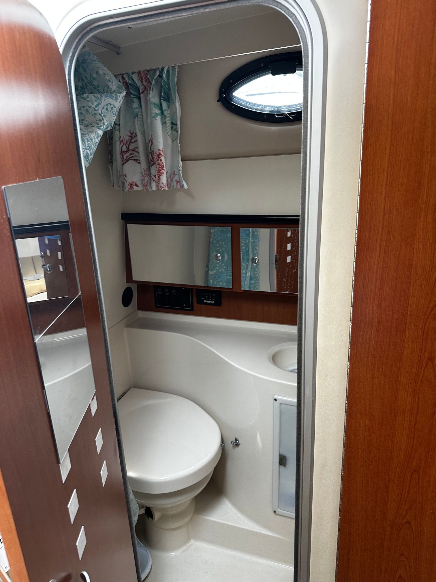 View into a yacht bathroom with toilet, mirror, and porthole.