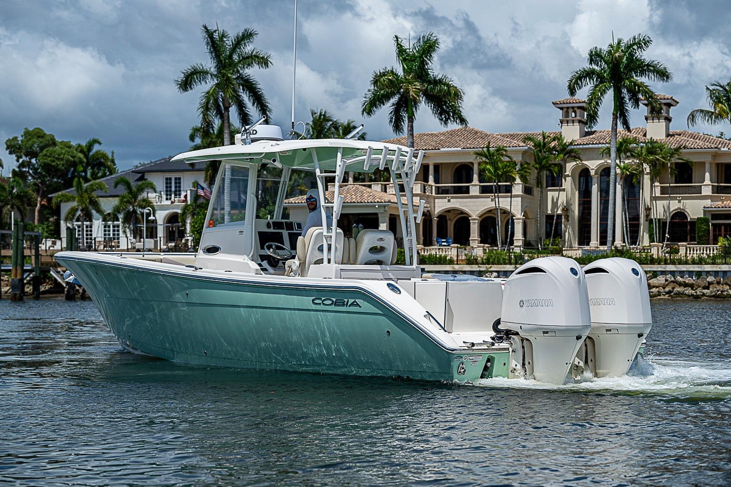 2019 Cobia 320 Center Console boat cruising near luxury waterfront homes.