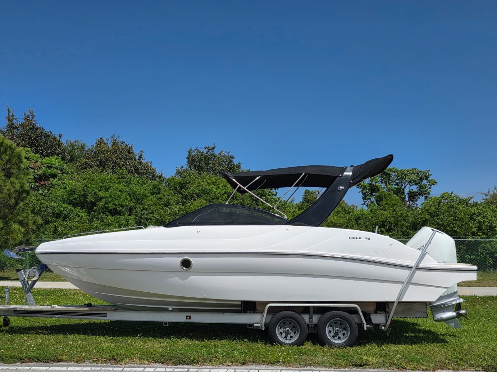 A white Coral 26 boat on a trailer, set against a green backdrop.