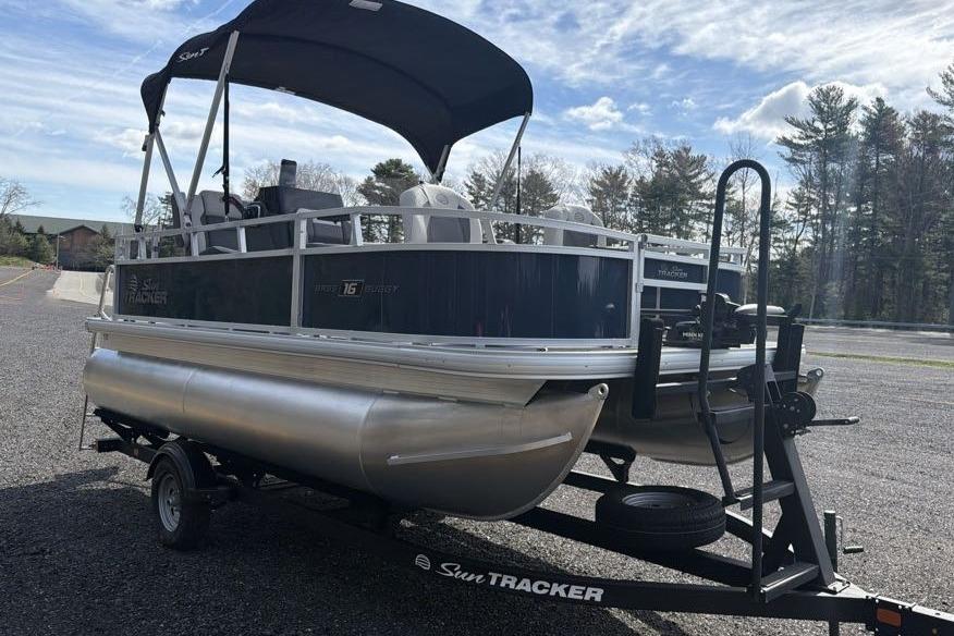 2026 Sun Tracker Bass Buggy 16 XL Select pontoon boat on trailer, parked outdoors.