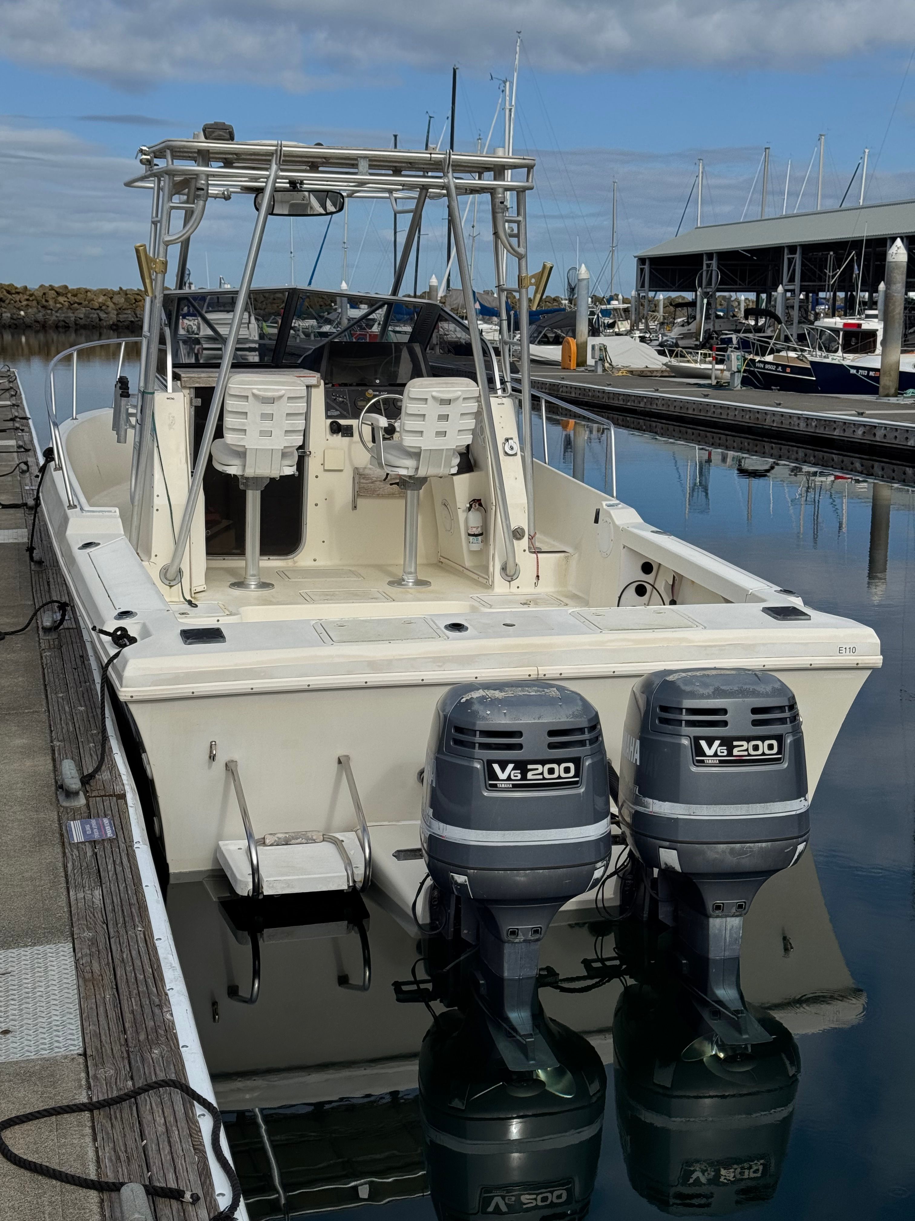 A boat with two outboard engines docked in a marina. It features two seats and a helm.