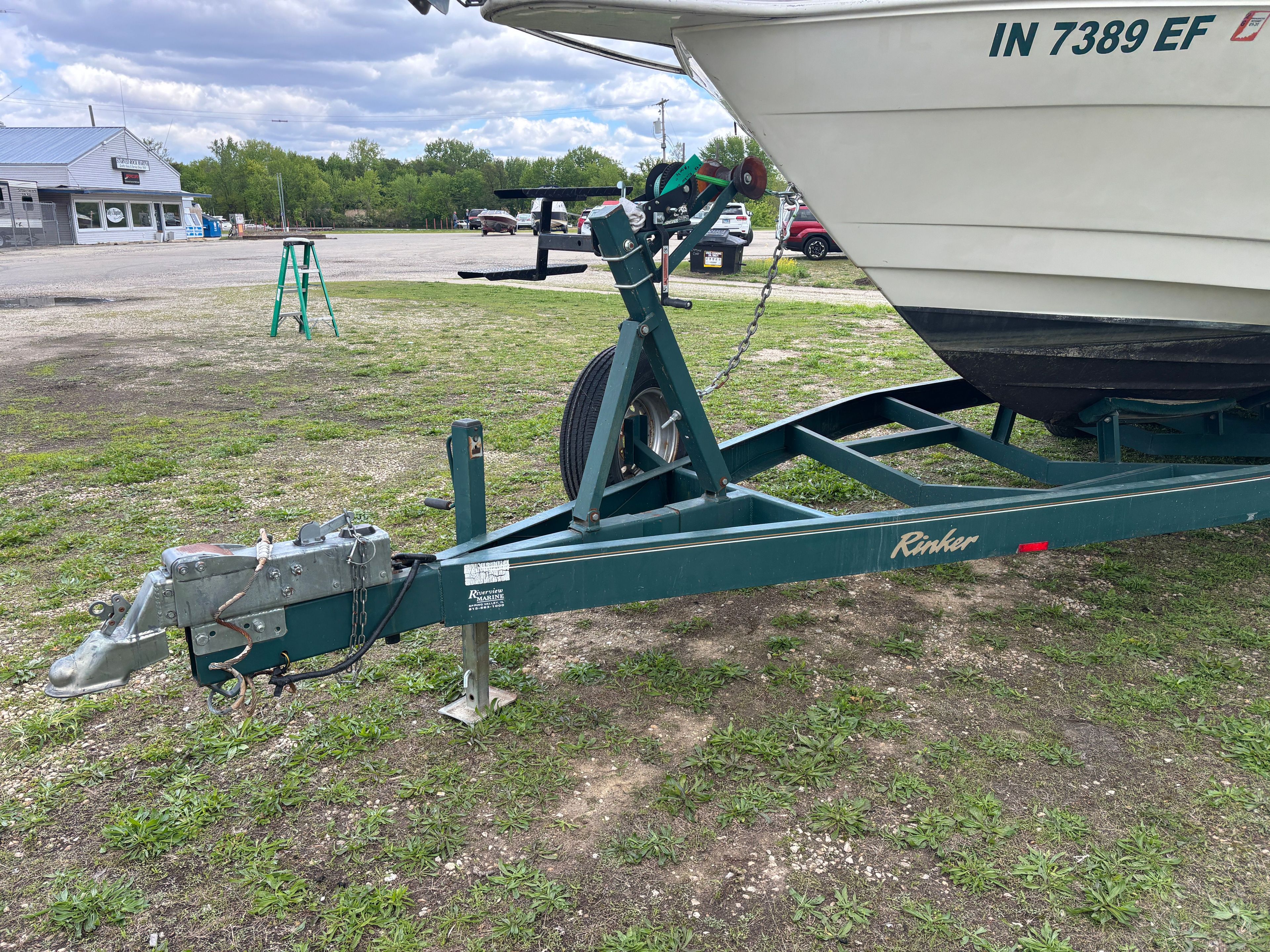A boat on a trailer in a parking area with grass and buildings in the background.