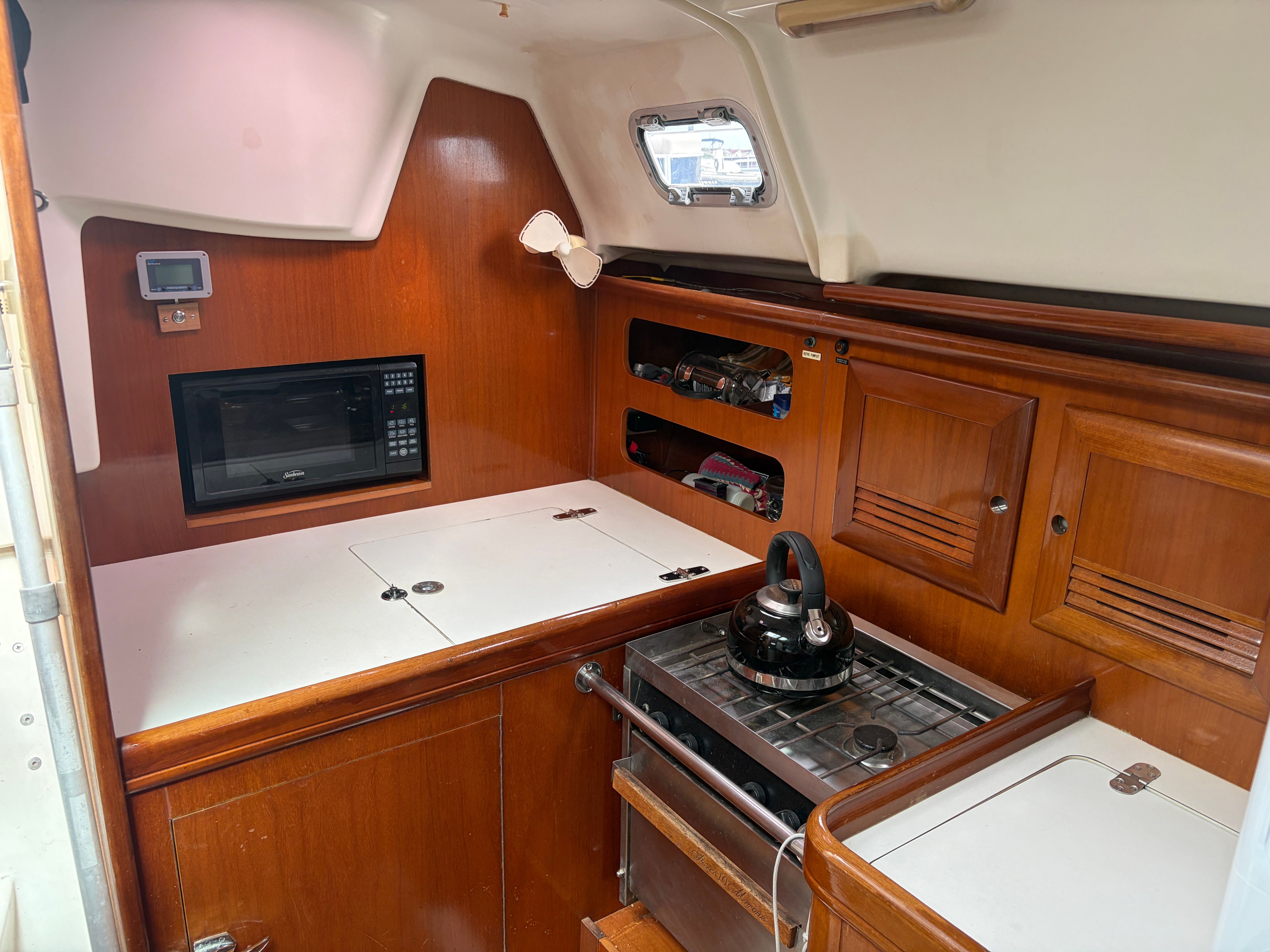 Galley of the Beneteau Oceanis 361 with wooden cabinets, stove, microwave, and kettle.