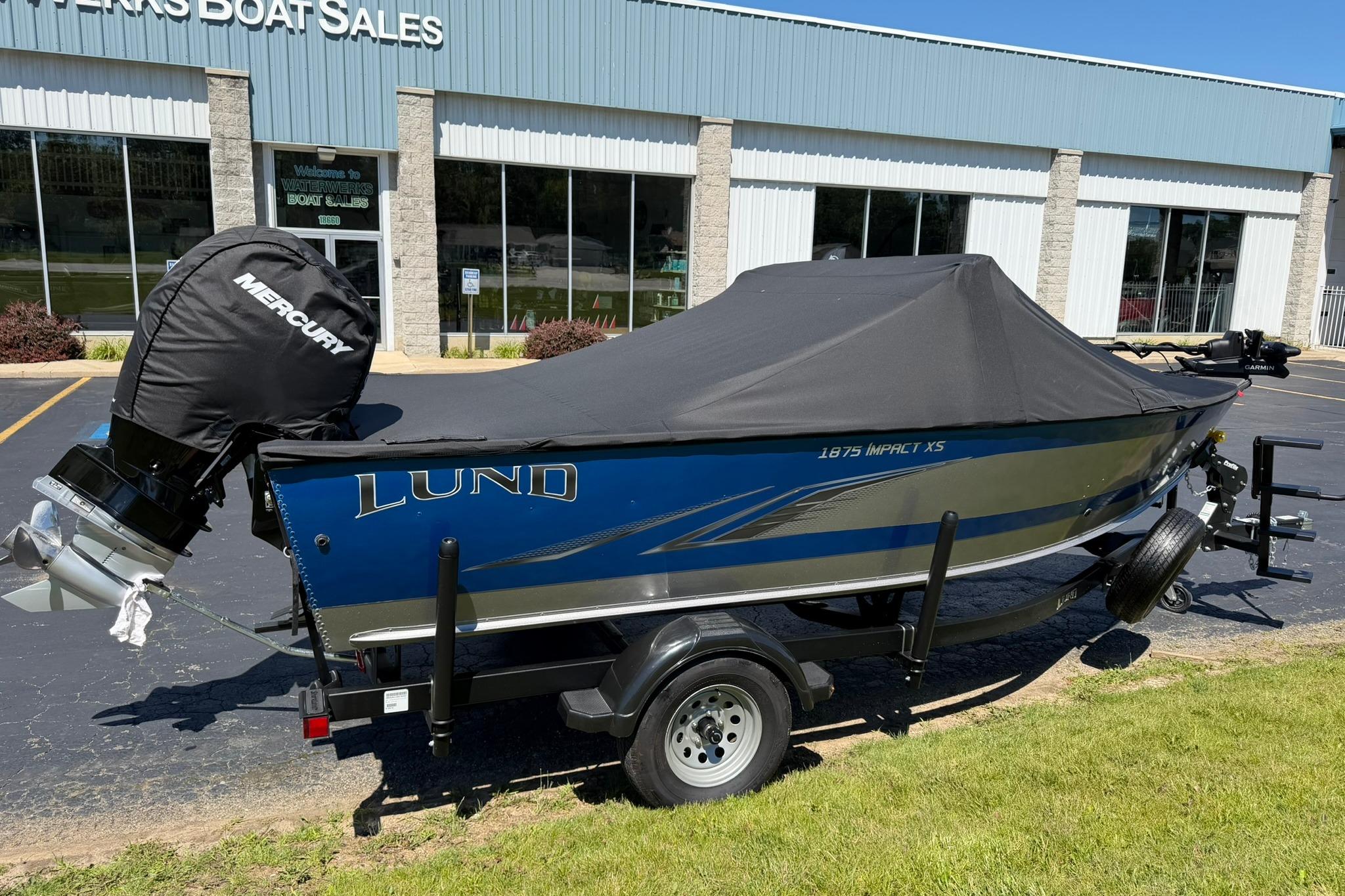 2024 Lund 1875 Impact XS Sport boat with cover, parked outside dealership.