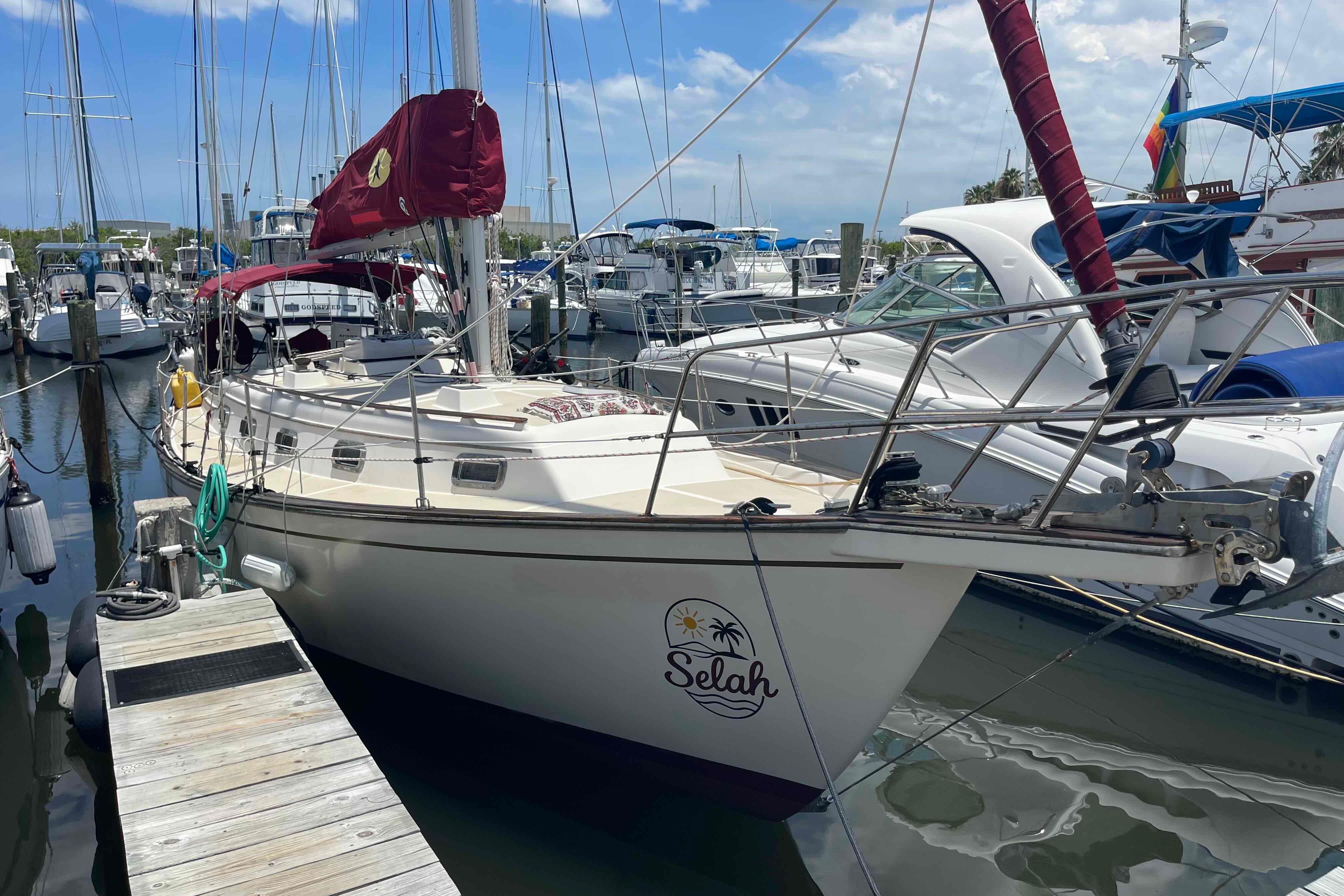 1989 Island Packet 35 sailboat docked at marina, featuring maroon sails and "Selah" logo.