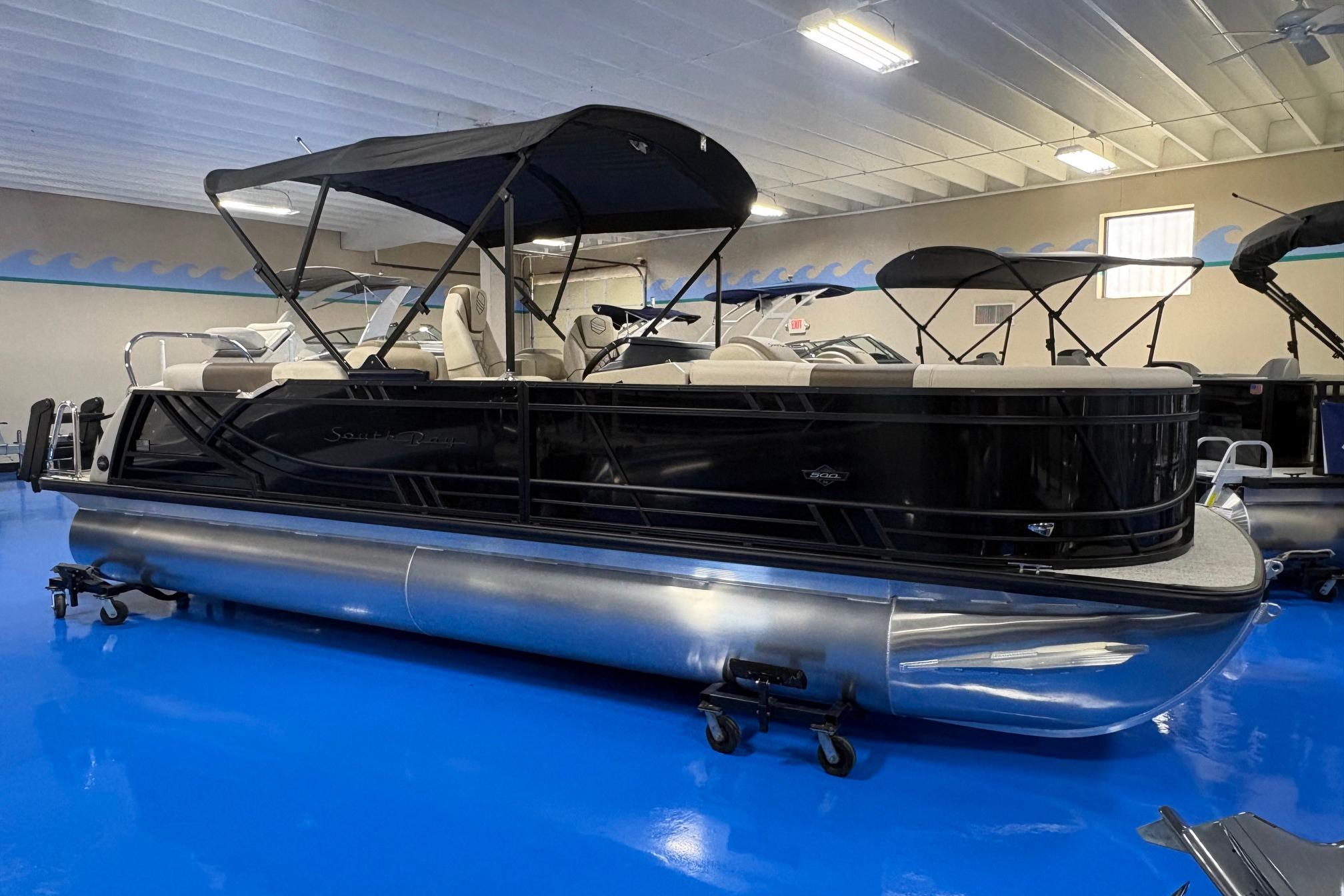 2026 South Bay 523RS pontoon boat in showroom with blue flooring and black canopy.