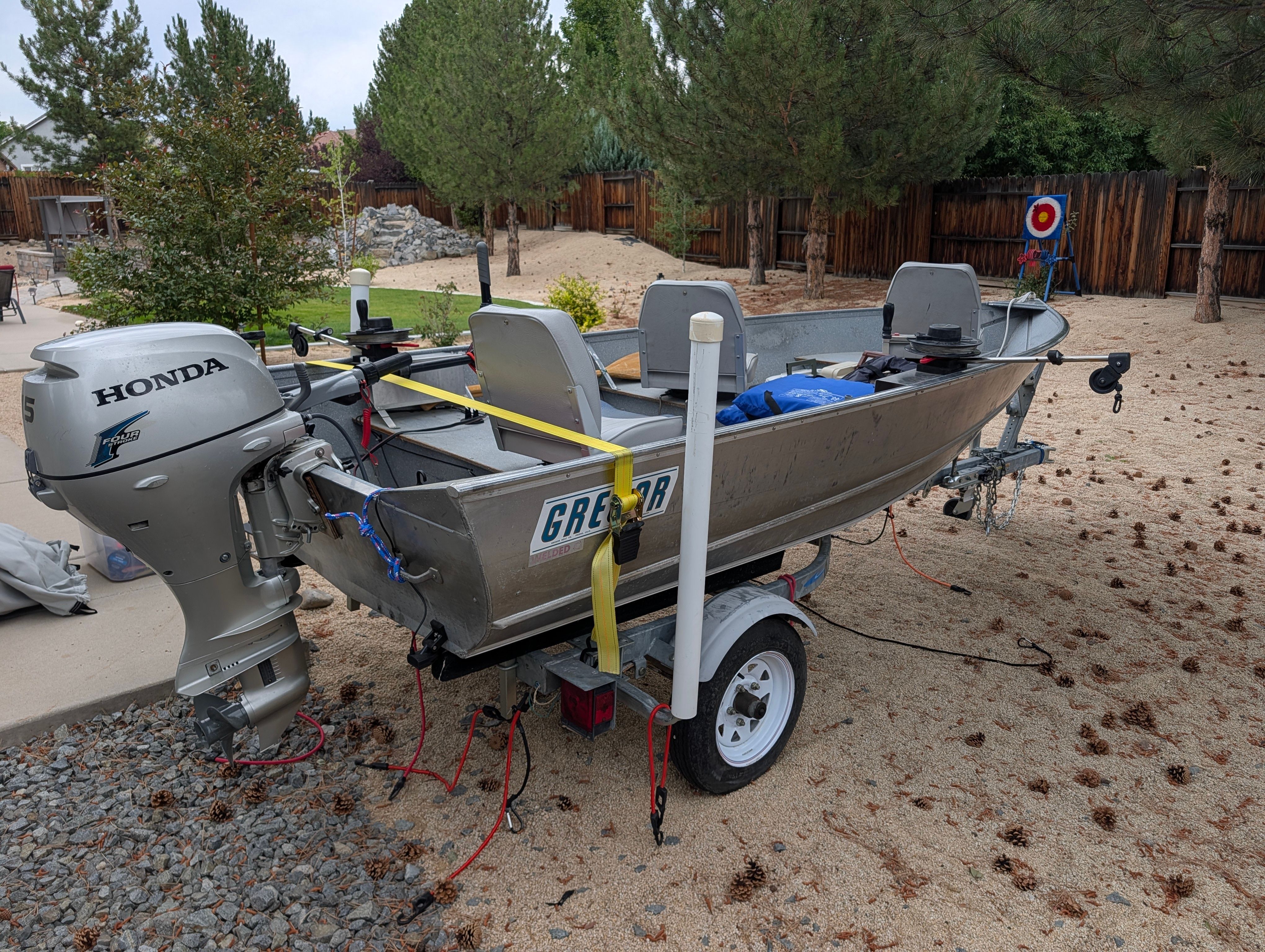 A silver 2004 Gregor Jon boat on a trailer in a backyard setting.