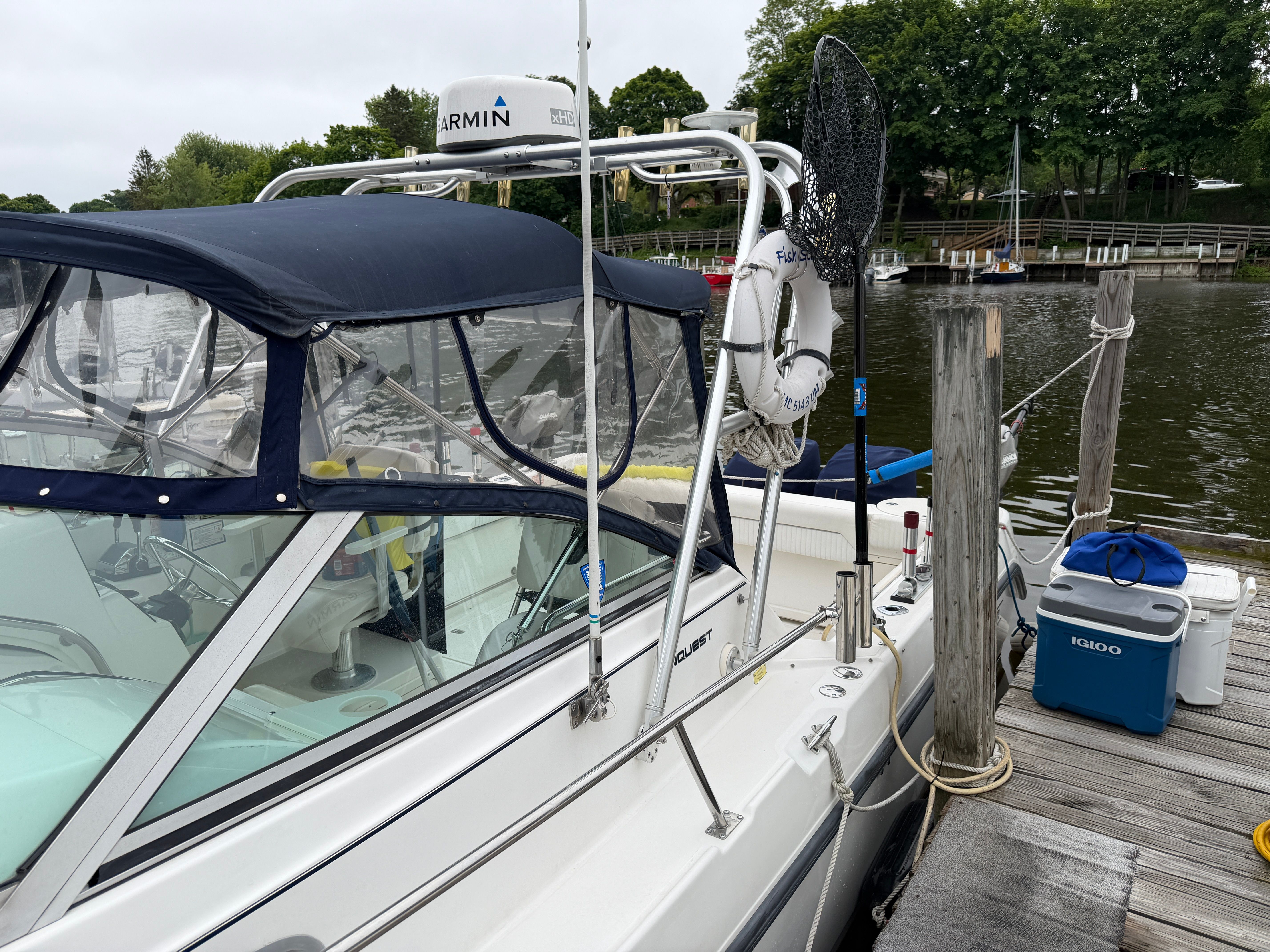 A 2001 Boston Whaler 26 Conquest docked at a wooden pier. It features a blue canopy.