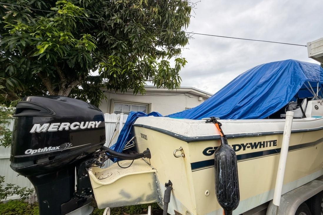 1989 Grady-White Offshore 242 boat with Mercury OptiMax engine, covered with blue tarp.