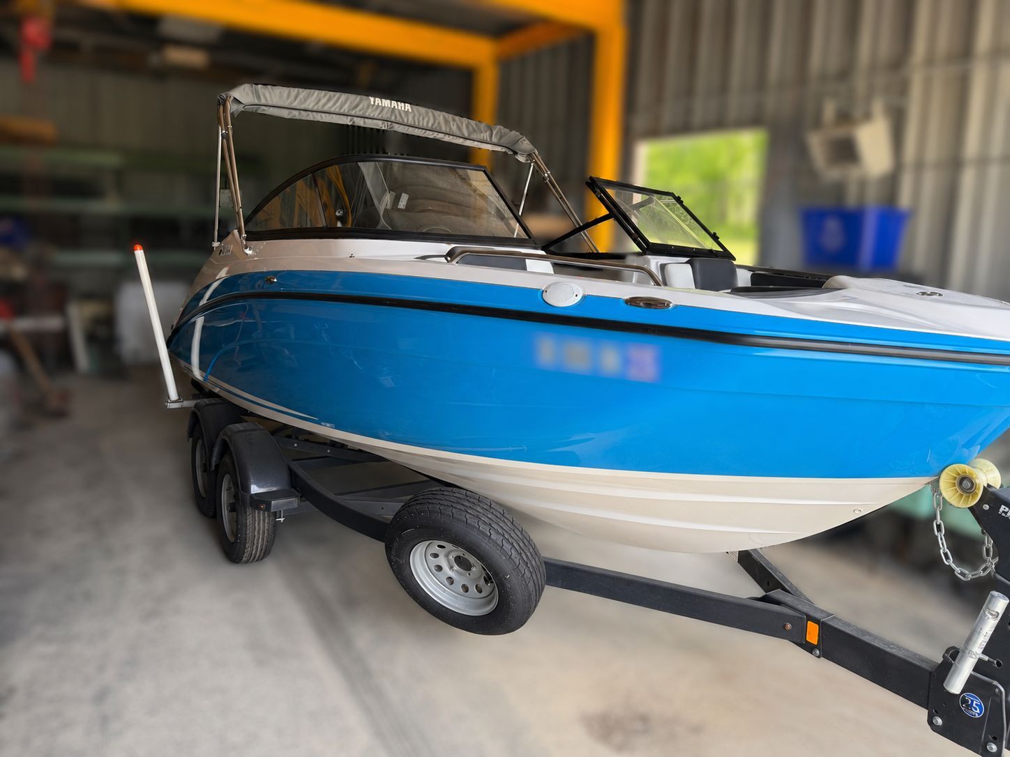 A blue and white 2021 Yamaha SX210 boat on a trailer inside a storage facility.