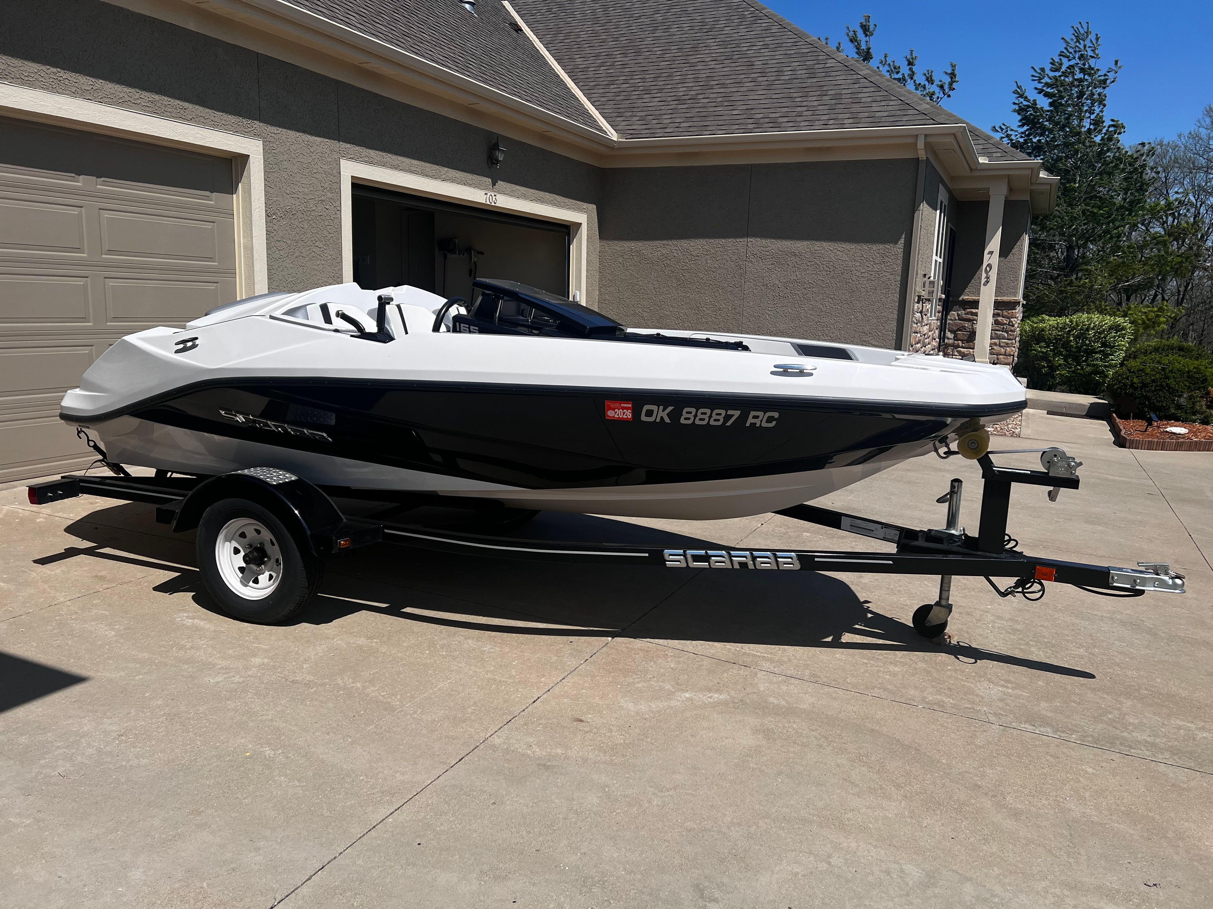 A white and black Scarab boat on a trailer in a driveway.