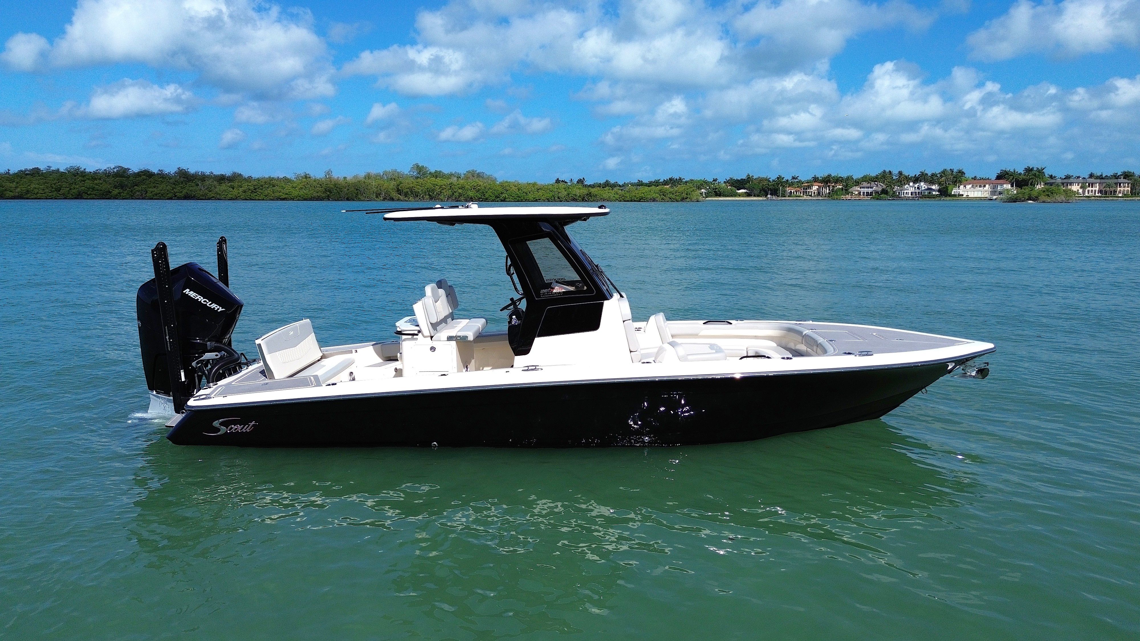 2024 Scout 281 XSS on calm water with blue sky and shoreline in the background.