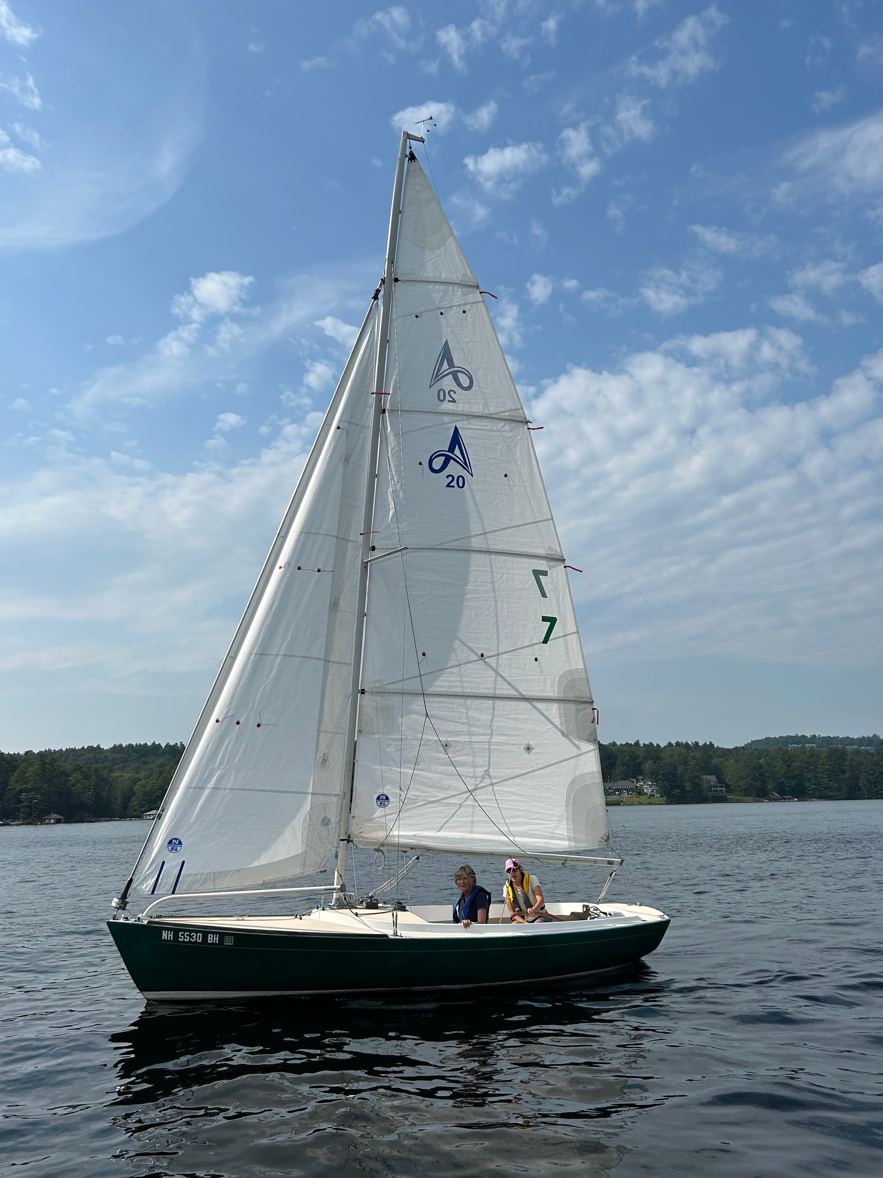Two people sailing an Alerion Express 20 on a calm lake.