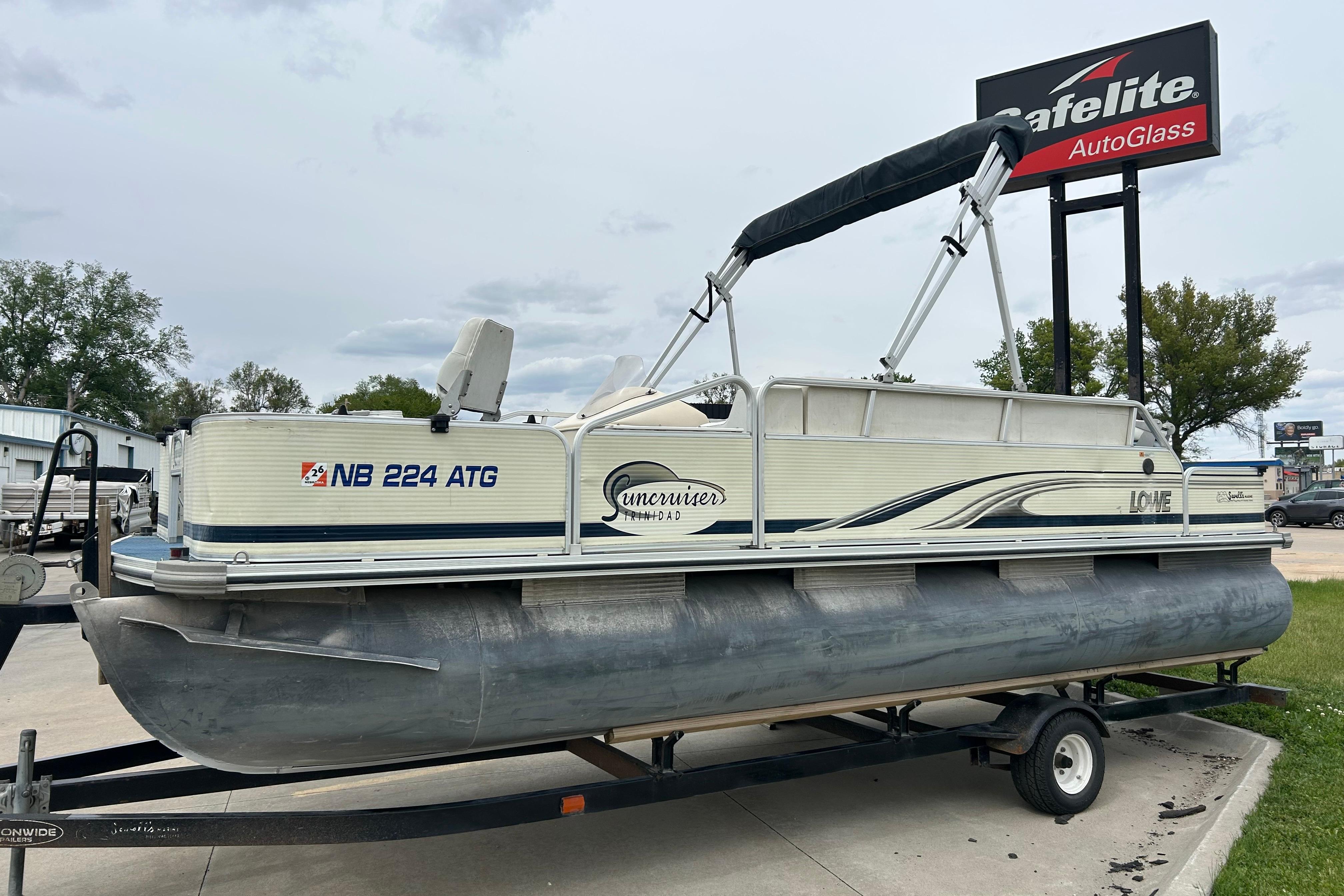 2002 Lowe Trinidad 200 pontoon boat on trailer, parked near Safelite AutoGlass sign.