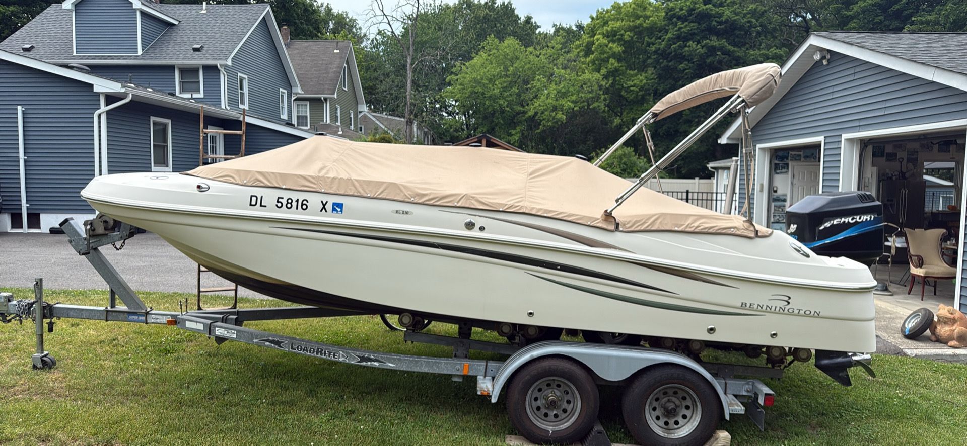 A 2004 Bennington RL210 boat on a trailer, covered, parked in front of a house.