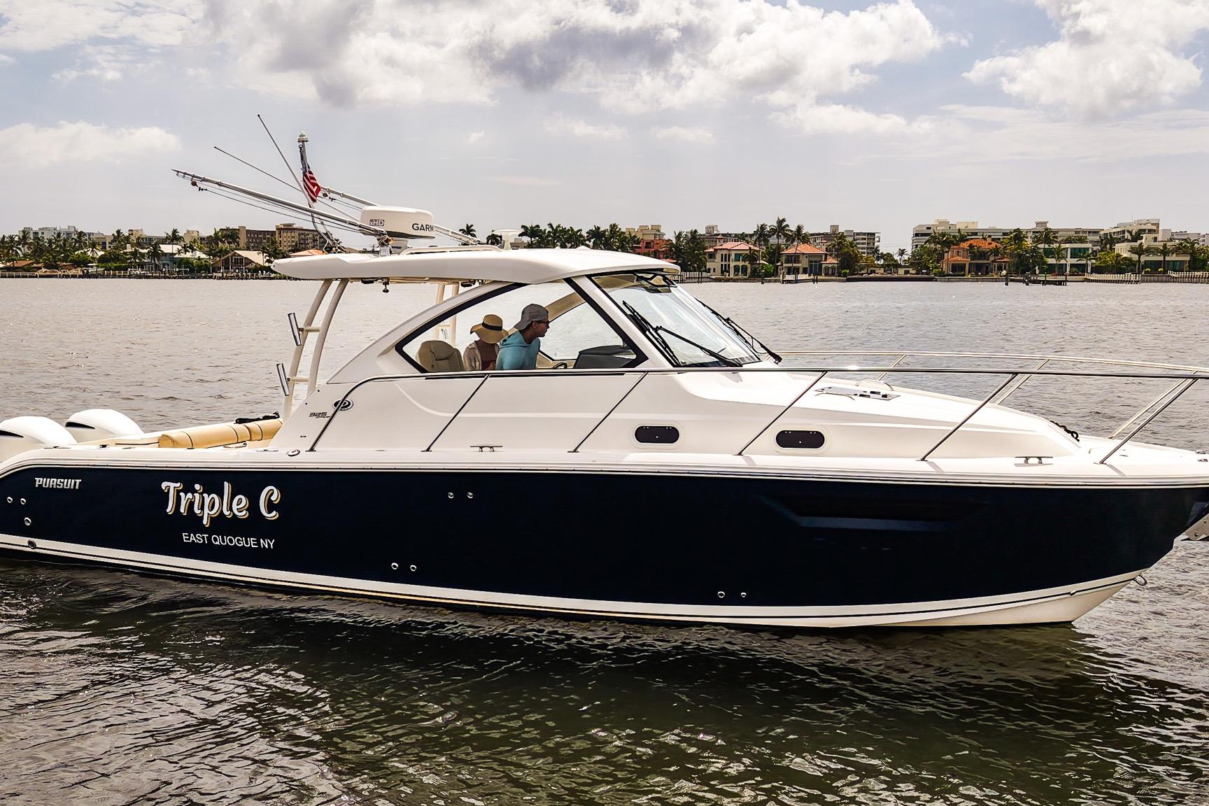 2020 Pursuit OS 325 Offshore boat cruising on calm waters near a coastal city.