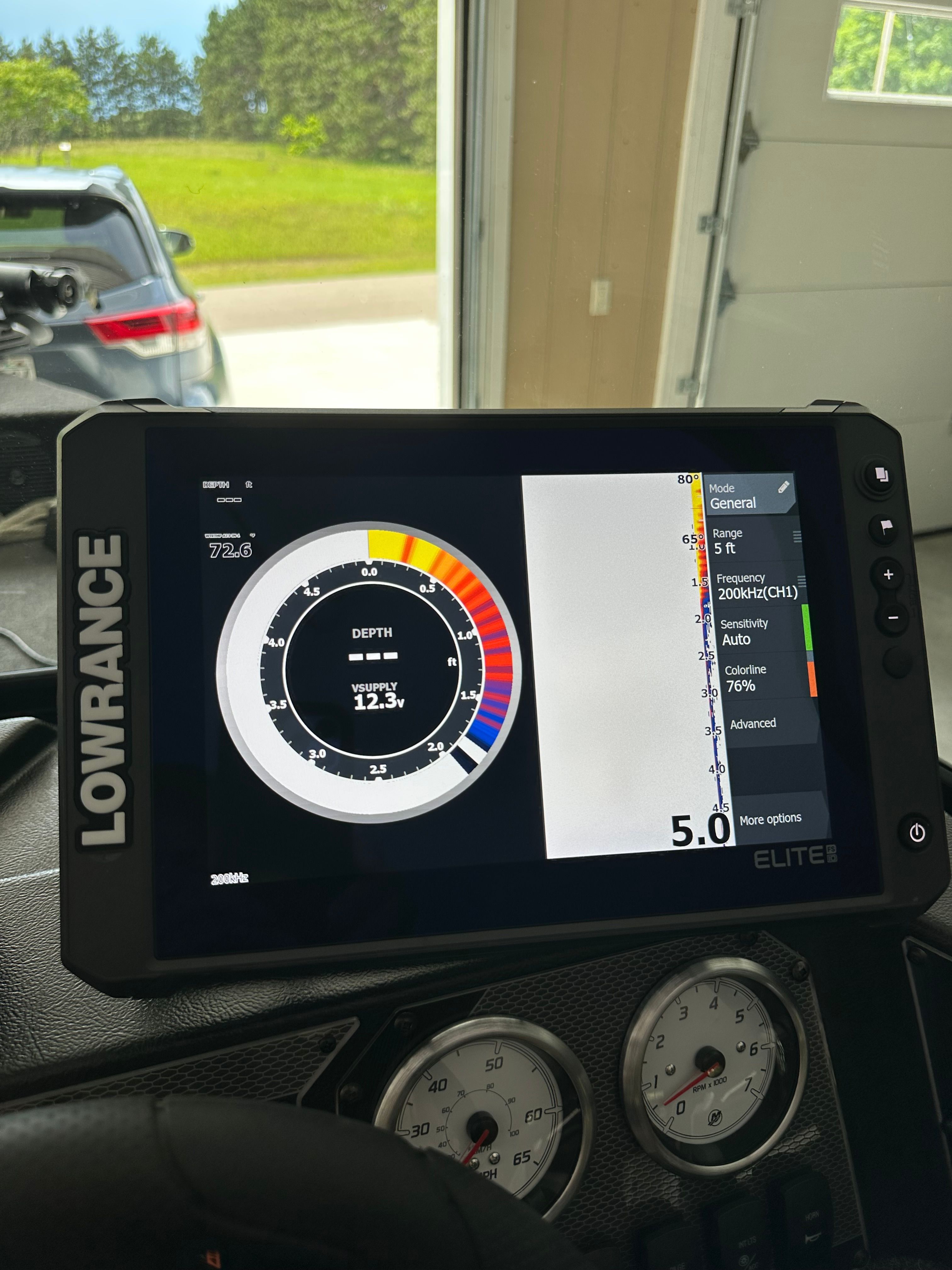 A Lowrance Elite fish finder displays depth and speed data. A garage is visible in the background.