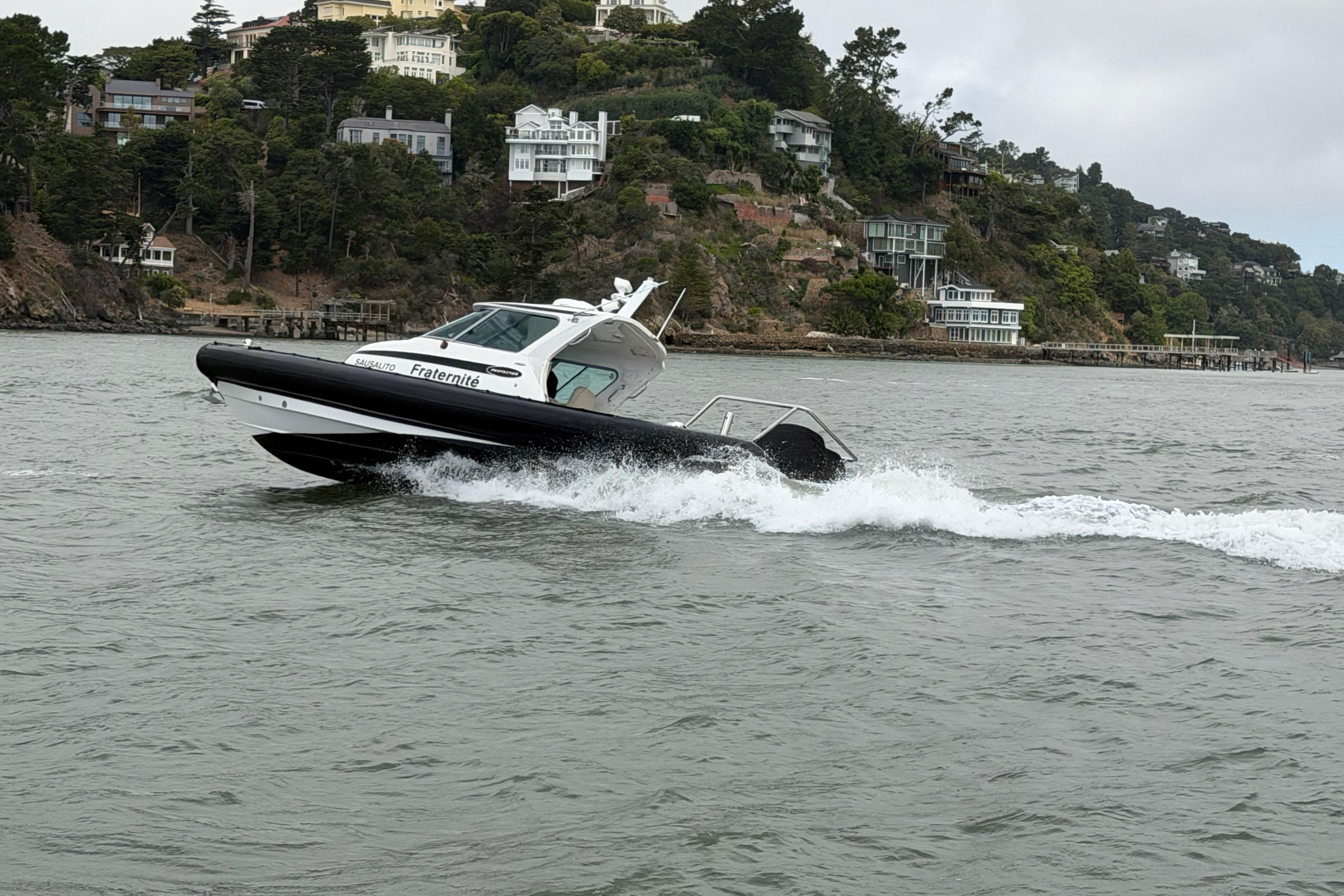 2016 Protector Targa 30 boat cruising near a scenic coastal area with hillside homes.