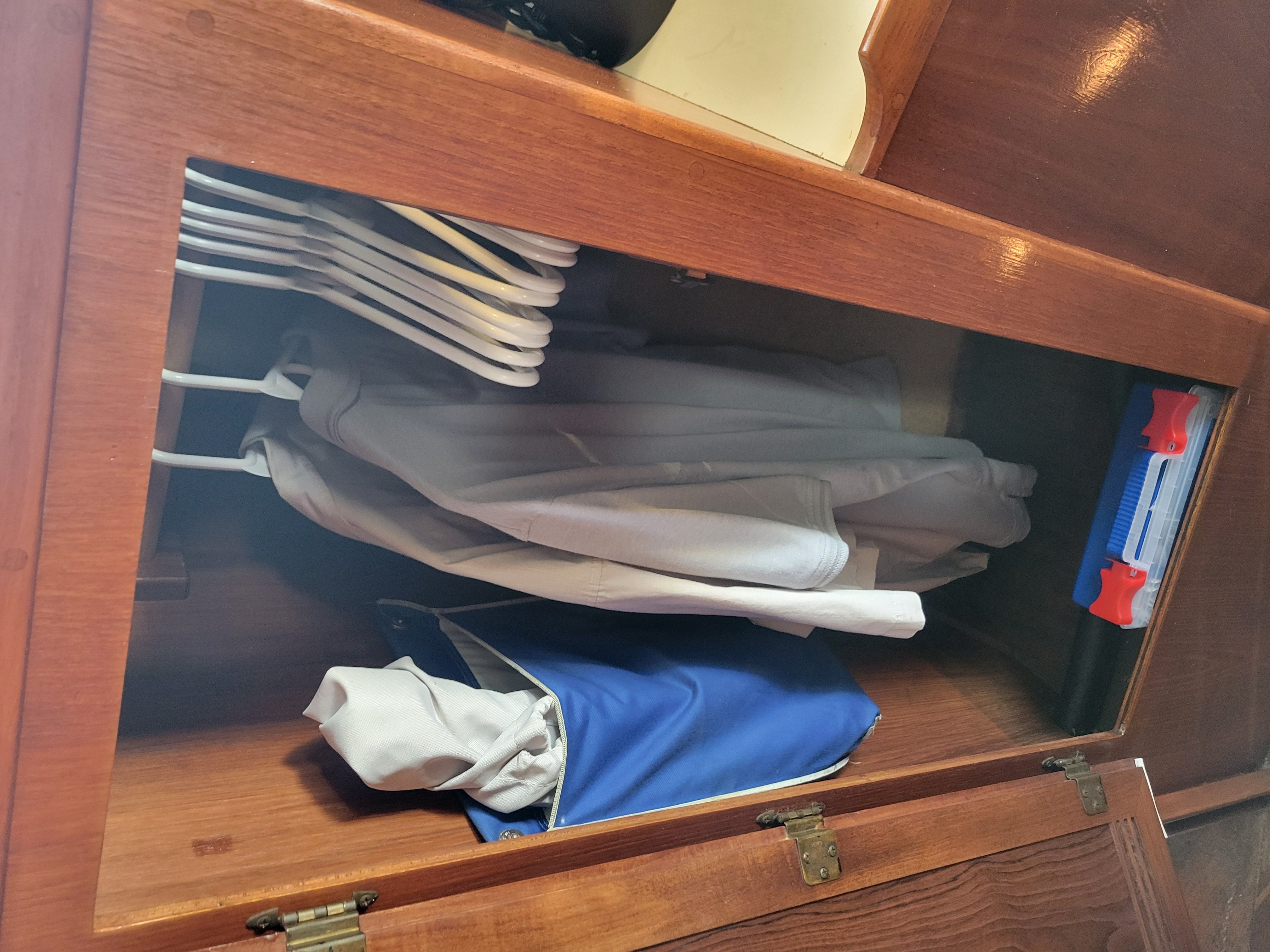 A wooden cabinet with clothes and hangers inside.